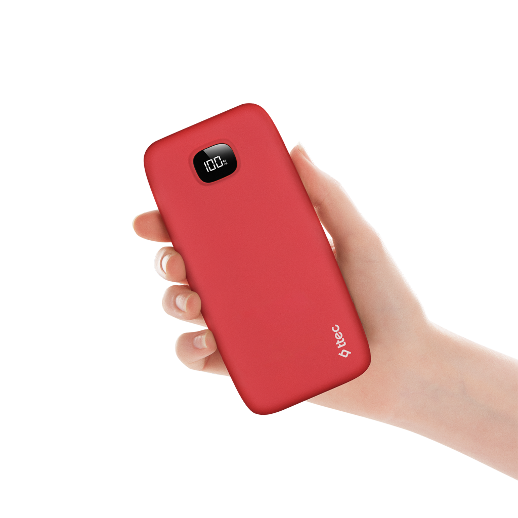 Bir el kırmızı bir powerbank tutuyor. Ekran %100 gösteriyor. Arka plan kahverengi ve beyaz karelerin karışımıdır.