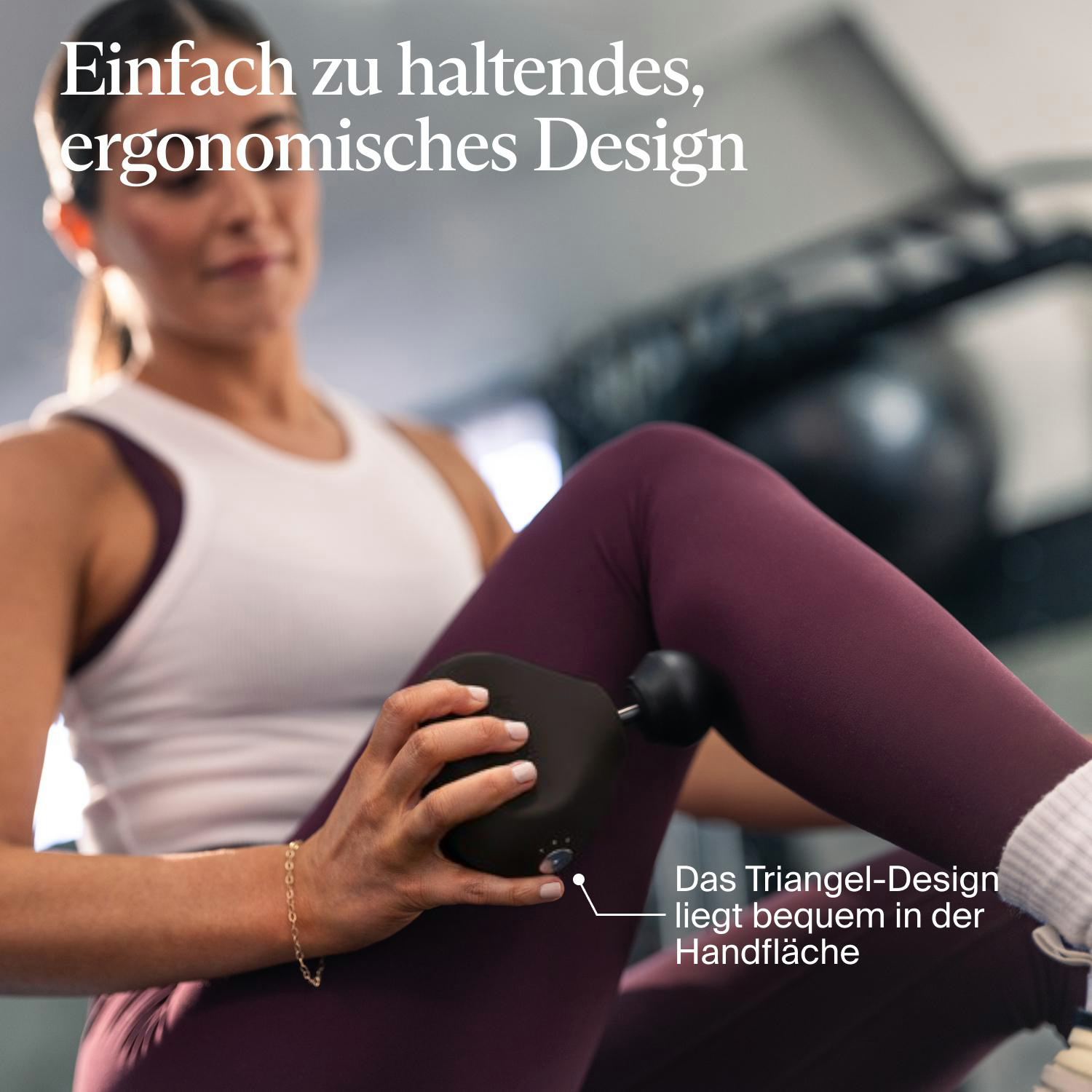 Eine Frau benutzt eine schwarze Massagepistole an ihrem Bein. Sie trägt ein weißes Tanktop, lila Leggings und ein goldenes Armband.