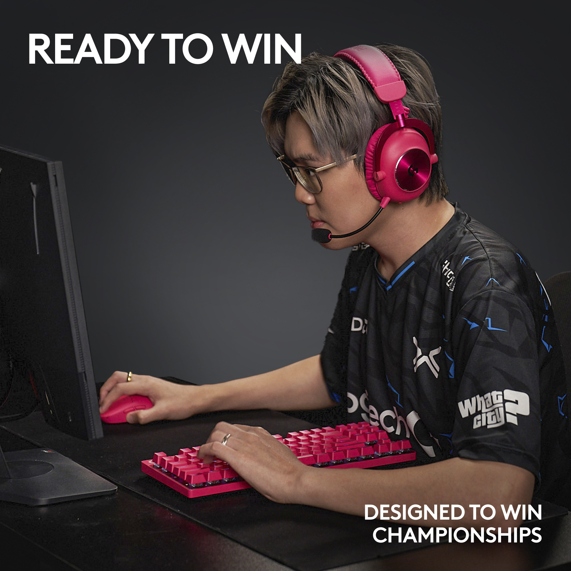 Un joueur avec un casque et un clavier roses joue devant un moniteur, portant des lunettes.