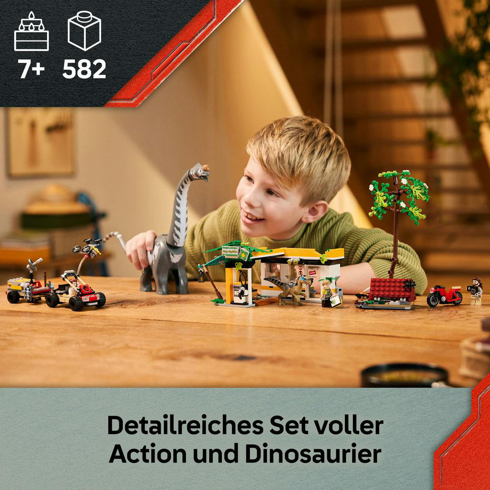 Ein Junge lächelt ein Spielzeug-Dinosaurier und ein Bauset an. Auf einem Holztisch befinden sich Spielzeugautos, Bäume und andere Gegenstände.
