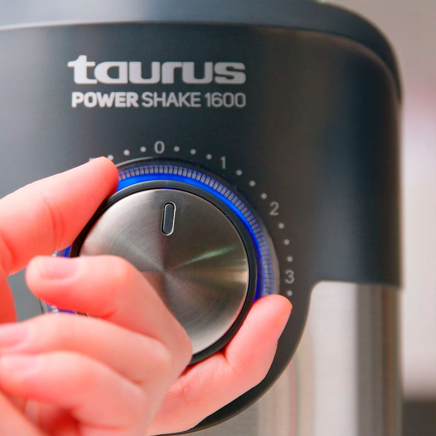 Una mano gira el dial de una licuadora Taurus Power Shake 1600. El dial está en la posición cero, con luz azul.