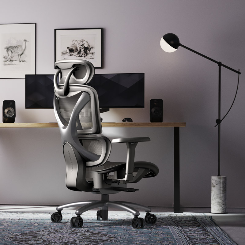 Sedia ergonomica in un ambiente ufficio moderno. Sono visibili monitor, altoparlanti e una lampada. Opere d'arte appese al muro. Un tappeto sul pavimento.