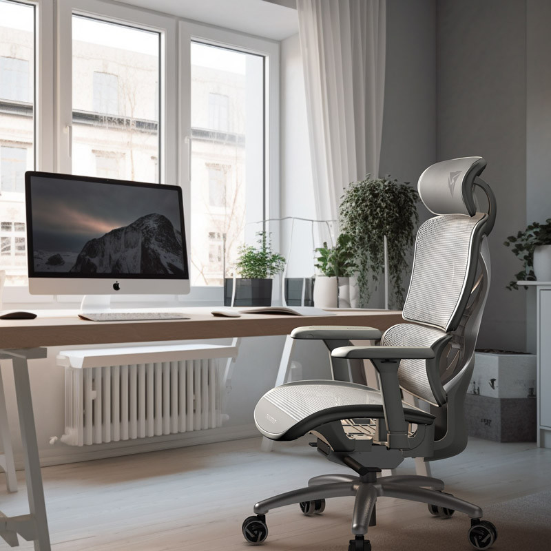 Interno ufficio con grande finestra, scrivania con computer e sedia ergonomica. Visibili piante e tende.