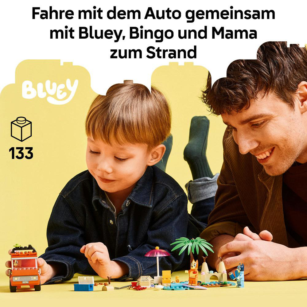 Ein Junge und ein Mann spielen mit Bluey-Spielzeugen. Die Szene umfasst Spielzeugauto- und Strandelemente. Beide lächeln.