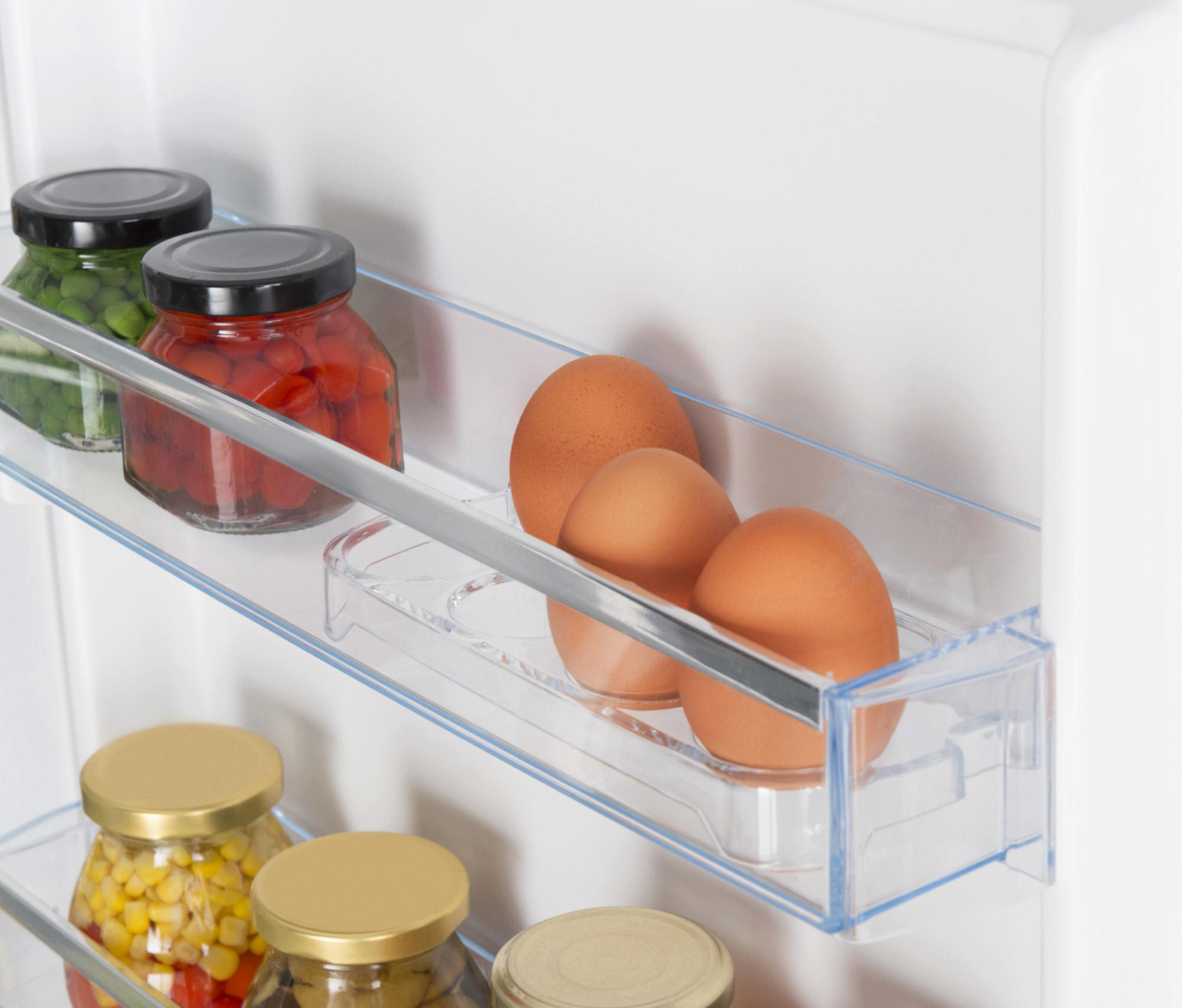 Im Kühlschrank: Gläser mit Lebensmitteln auf Regalen, Eier in einem Behälter. Grüne Erbsen, rote Paprika, Mais und braune Eier sind sichtbar.