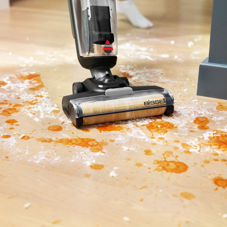 Odkurzacz Bissell czyści drewnianą podłogę z plamami. Podłoga ma czerwone i białe plamy.