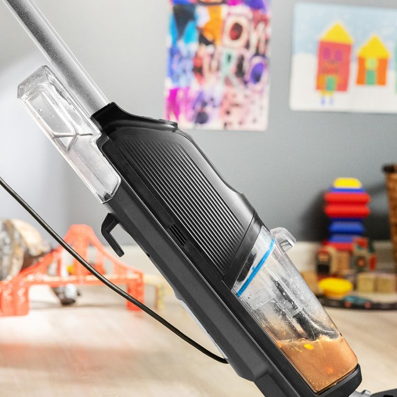 Czarny i przezroczysty odkurzacz z brudną wodą w pojemniku stoi na drewnianej podłodze. Kolorowe rysunki są w tle.