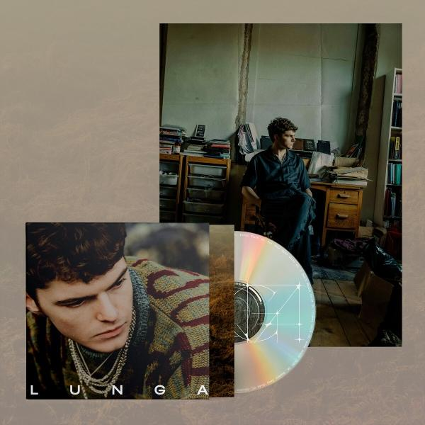 Ein Mann sitzt in der Nähe eines Schreibtisches. Eine CD und Albumcover befinden sich im Vordergrund. Das Albumcover zeigt das Gesicht des Mannes.