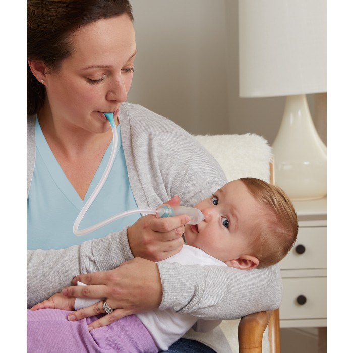 Kobieta używa aspiratora do nosa u dziecka. Dziecko jest trzymane w ramionach kobiety. Aspirator jest w nosie dziecka.