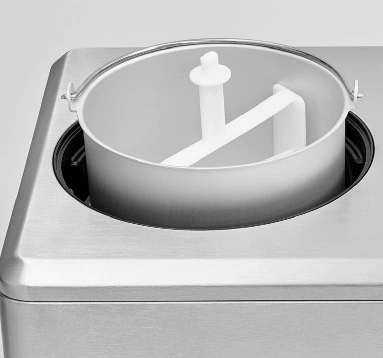 Maszyna do lodów z metalowym pojemnikiem i białą plastikową łopatką do mieszania. Maszyna jest srebrna i stoi na białej powierzchni.