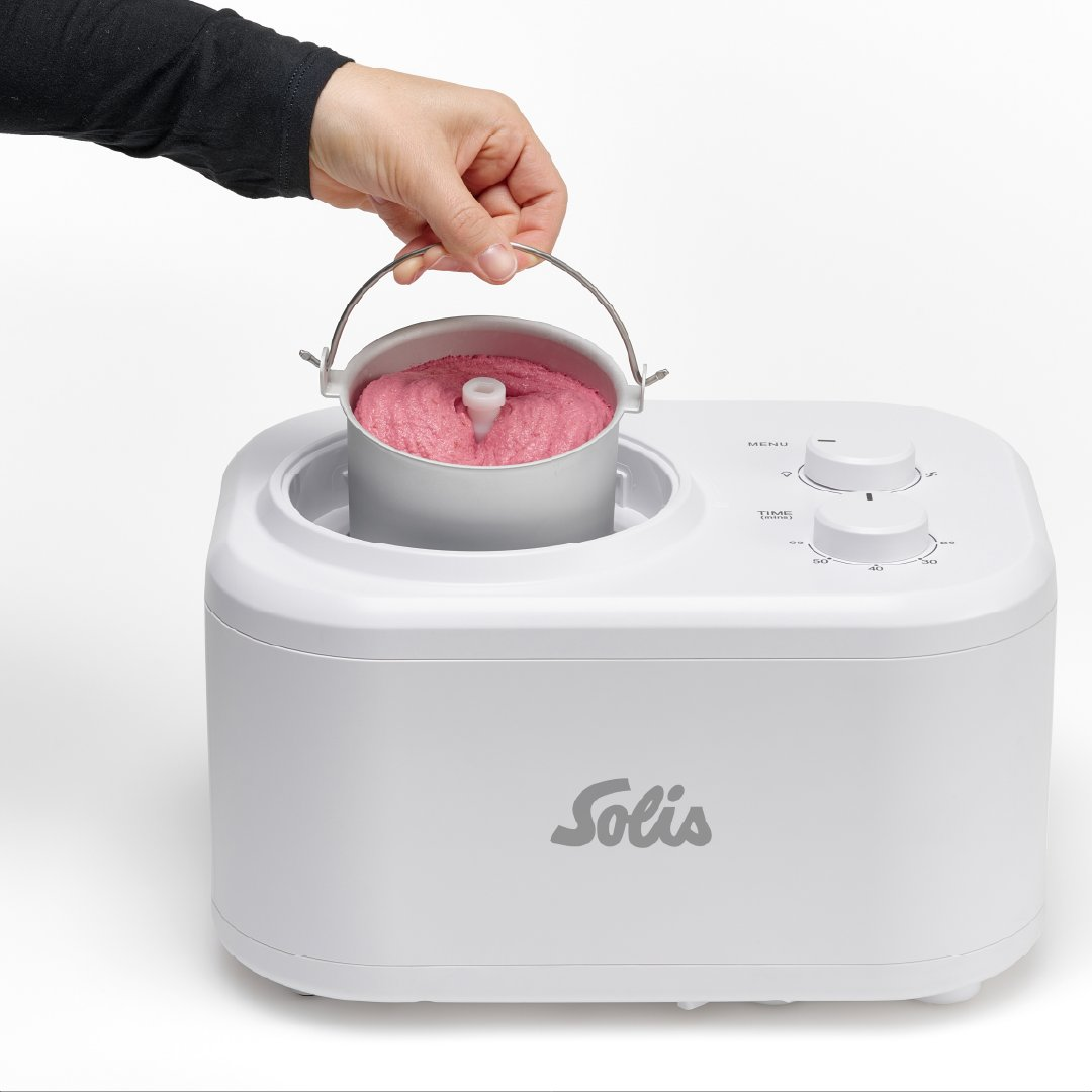 Ręka trzyma pojemnik z różowymi lodami z białej maszyny do lodów. Maszyna ma logo Solis.