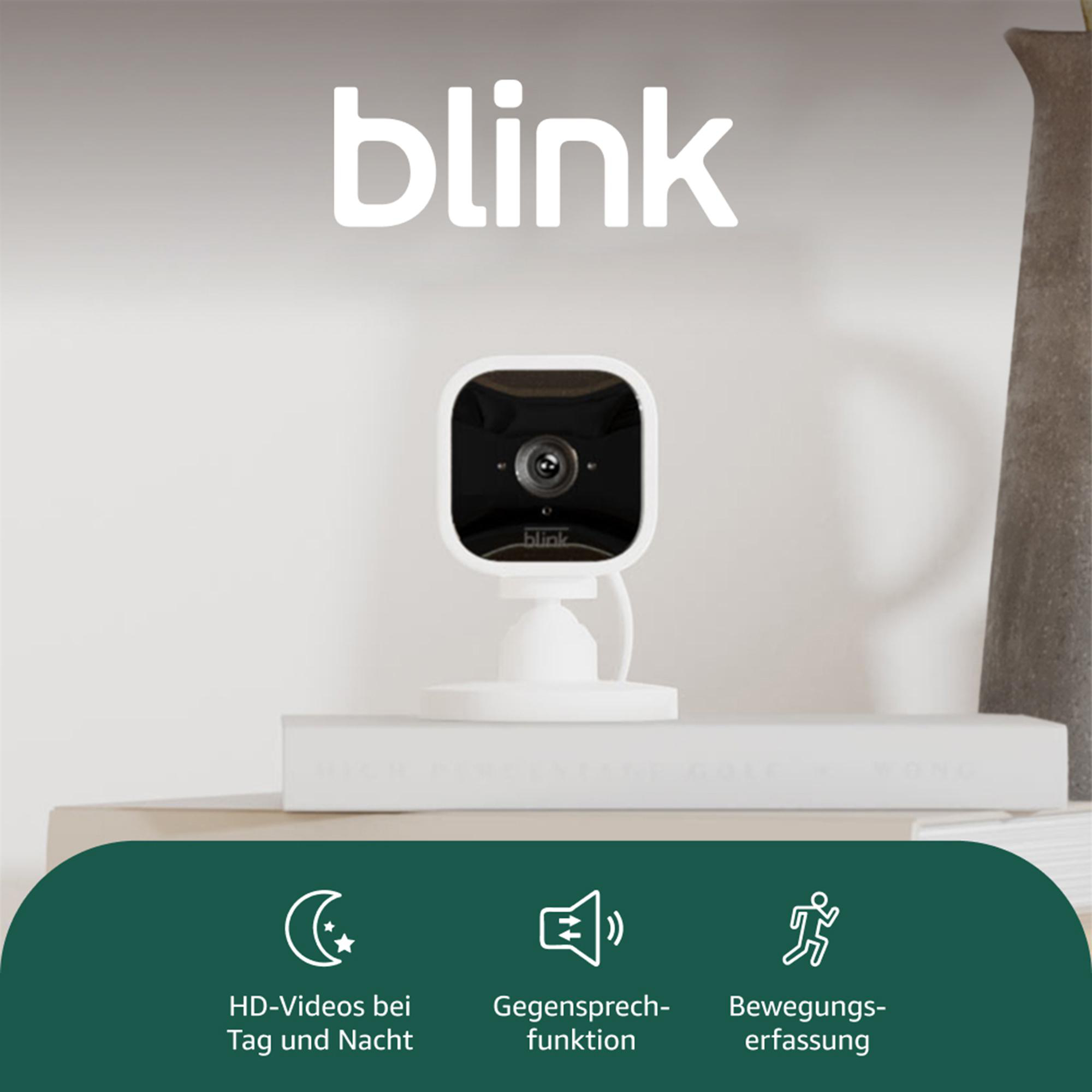 Eine weiße Blink-Überwachungskamera auf einem Regal mit Markenlogo. Funktionen: HD-Video, Zwei-Wege-Audio und Bewegungserkennung.