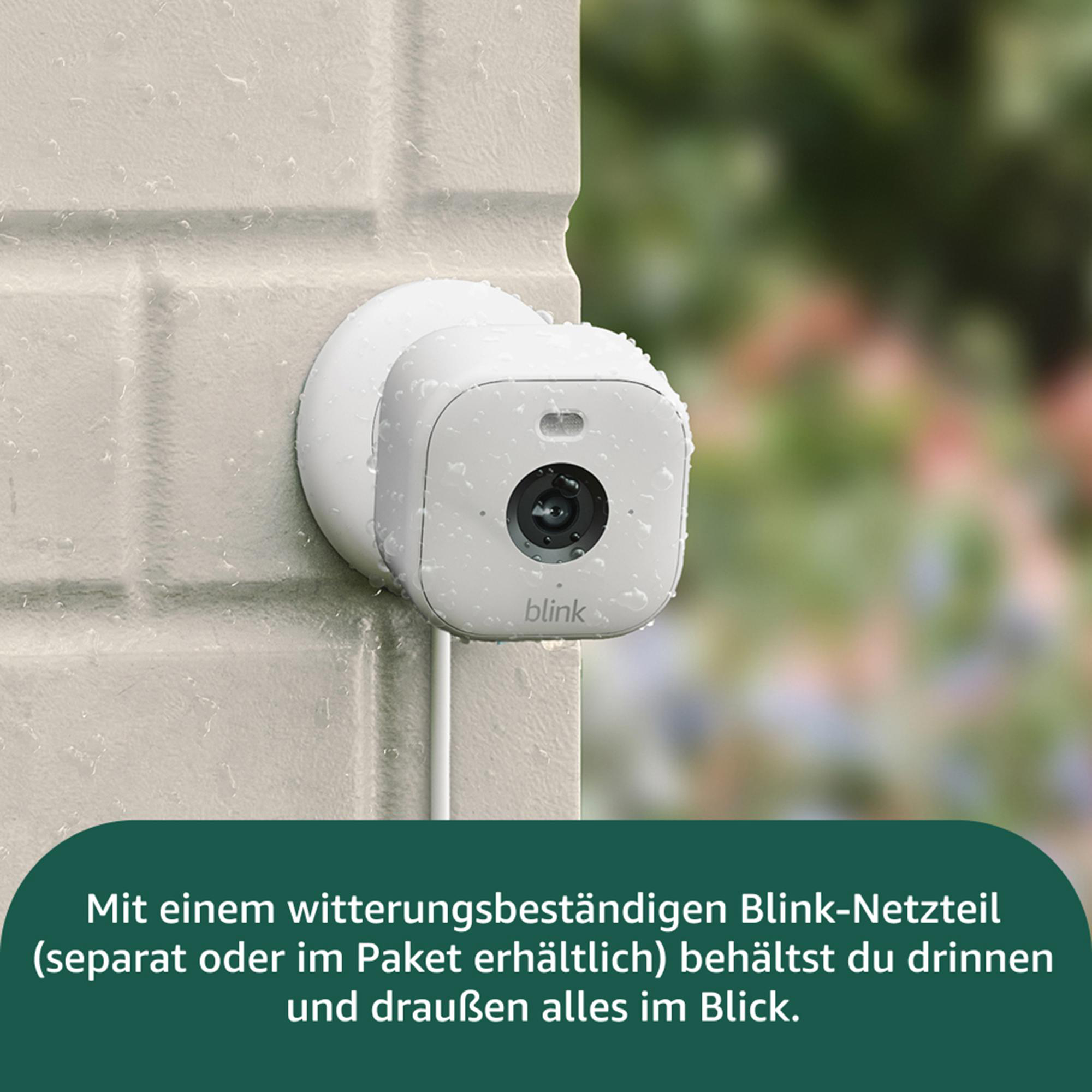 Eine weiße Überwachungskamera an einer hellen Ziegelmauer. Es regnet. Der Hintergrund ist verschwommen grün.