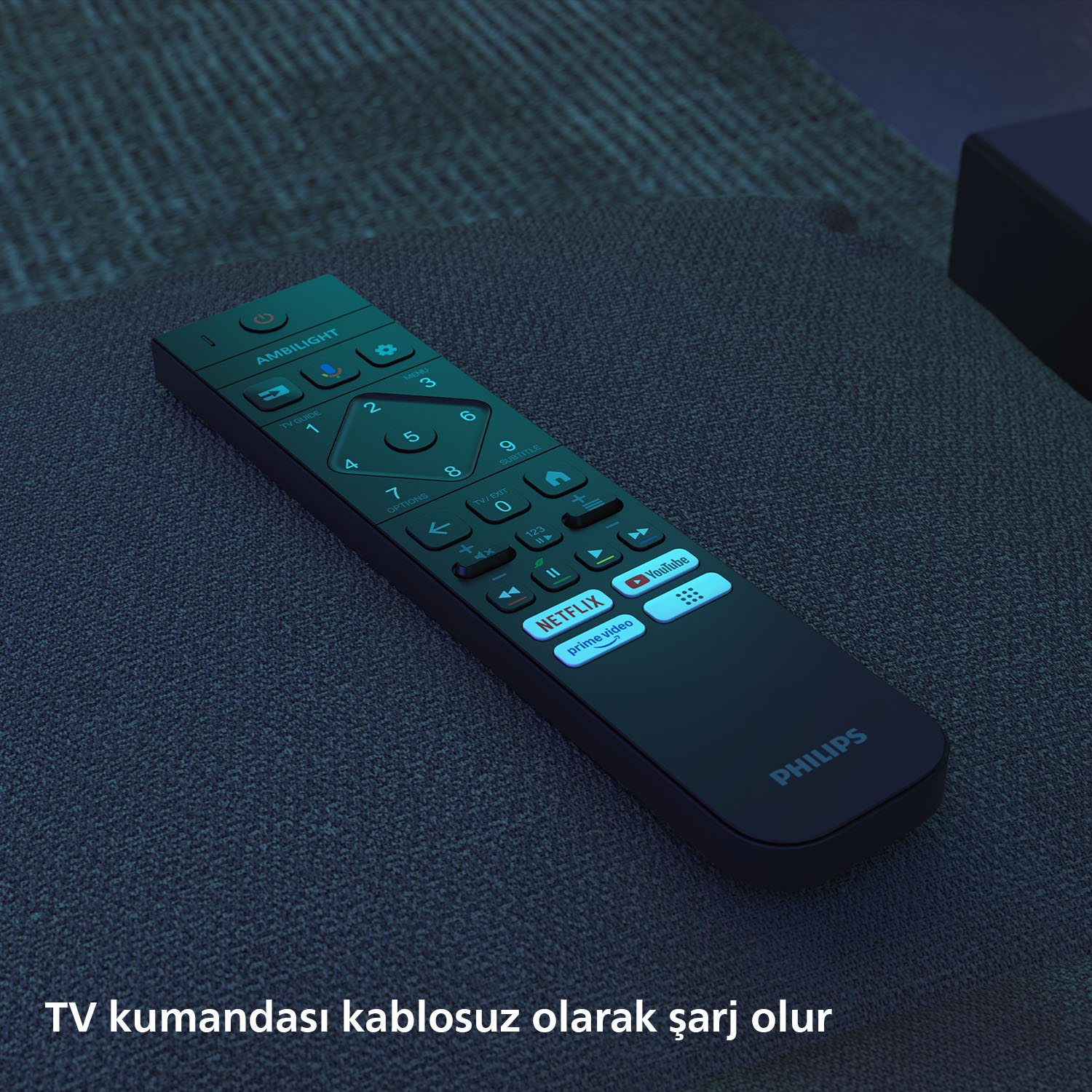 Siyah beyaz tuşlu bir Philips TV kumandası, koyu mavi bir kumaşın üzerinde duruyor. Kumandada Netflix ve Youtube düğmeleri var.