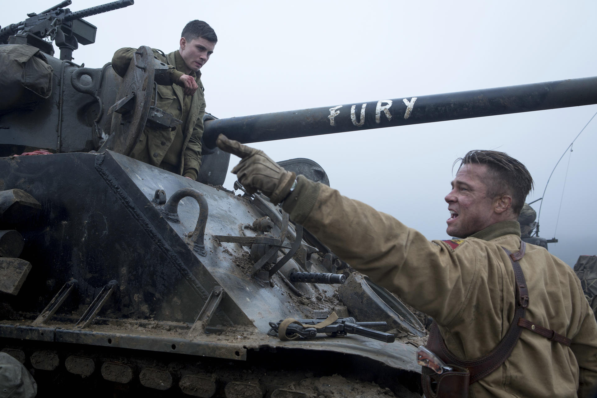 Soldaten auf einem Panzer. Einer zeigt, schreit. Ein anderer schaut zu. Eine Waffe ist sichtbar. Der Panzer sagt 'Fury'.