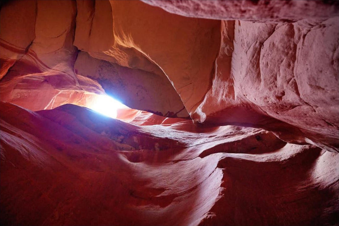Im Inneren eines roten Felsencanyons fällt Licht von oben ein. Die Wände sind glatt, gebogen und geschichtet. Die Szene ist beleuchtet.