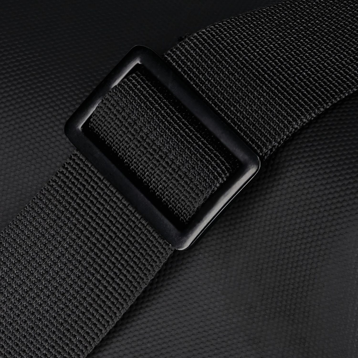 Gros plan d'une sangle noire avec une boucle noire, sur une surface noire texturée. La sangle est tissée.