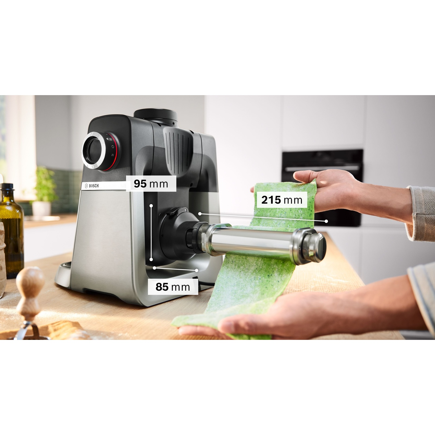 Viene mostrata una macchina per la pasta Bosch argento e nera. Si sta preparando pasta verde. Le dimensioni sono visualizzate sulla macchina.