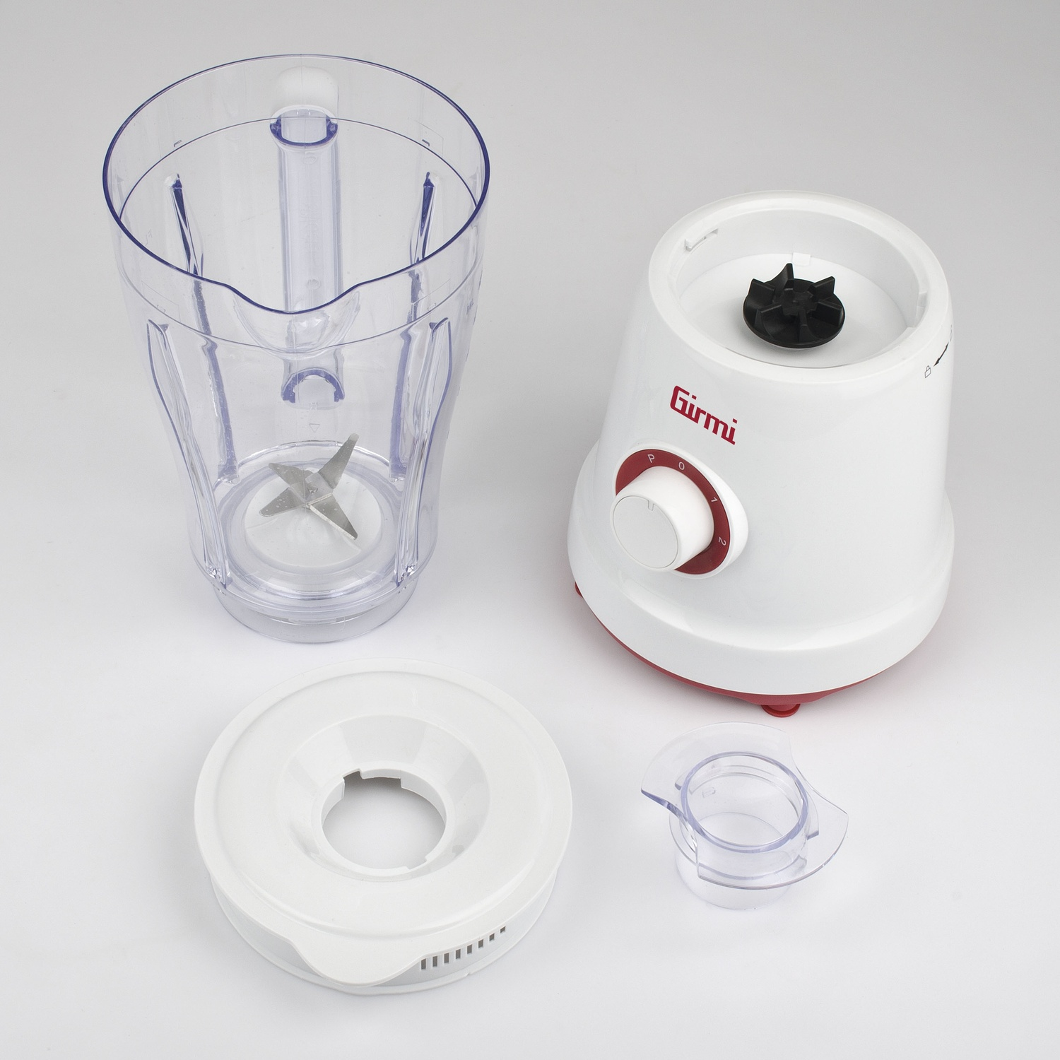 Un frullatore smontato con base bianca, caraffa trasparente, coperchio e piccolo contenitore. La base ha un quadrante rosso e una lama nera.