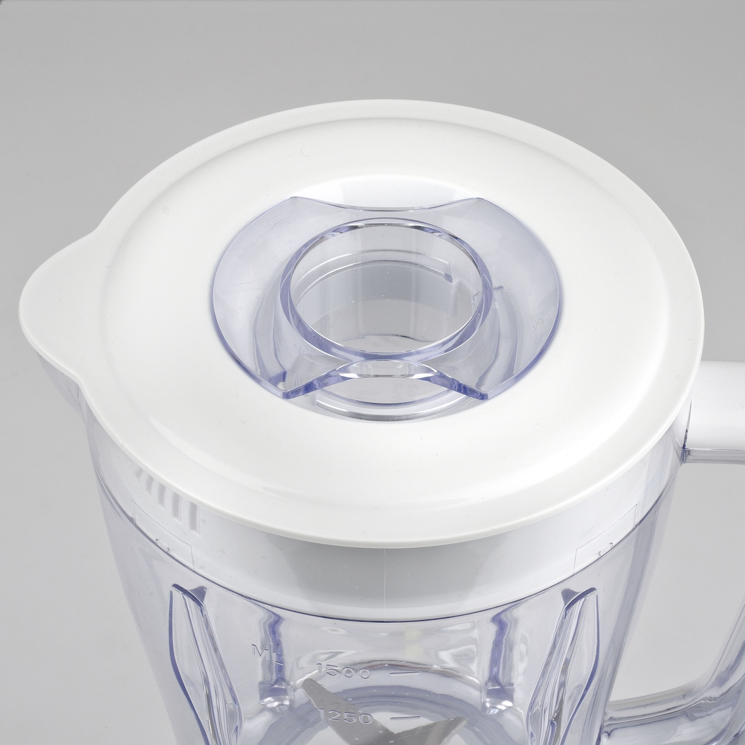 Primo piano di un frullatore. Ha un coperchio bianco con un centro trasparente e una caraffa di plastica trasparente con indicatori di misura.