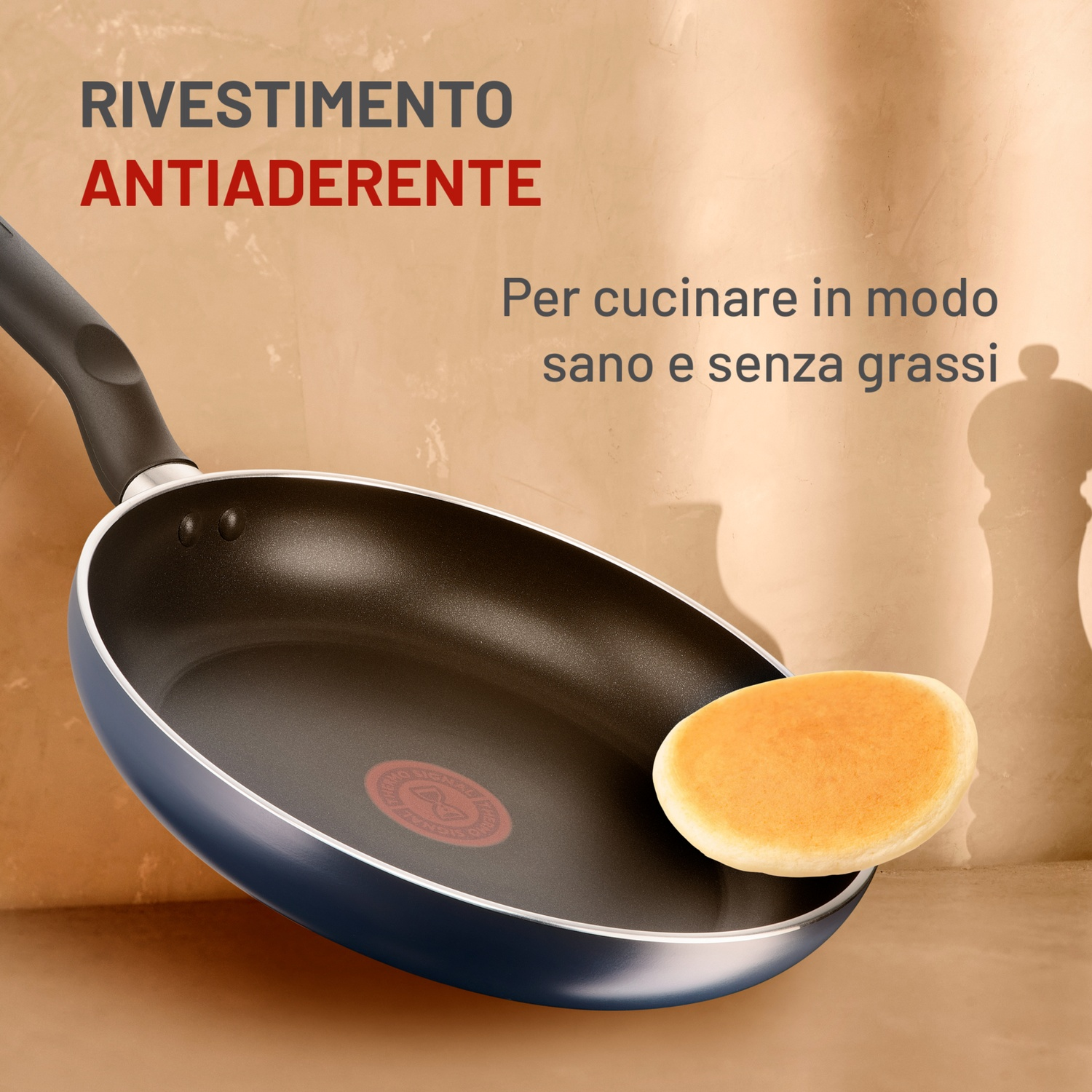 Una padella con un pancake all'interno. Il testo dice "Rivestimento antiaderente" e "Per cucinare in modo sano e senza grassi".