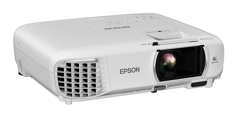 Beyaz bir Epson projektör. Bir lensi, havalandırmaları ve marka adı vardır. Beyaz bir yüzey üzerinde duruyor.