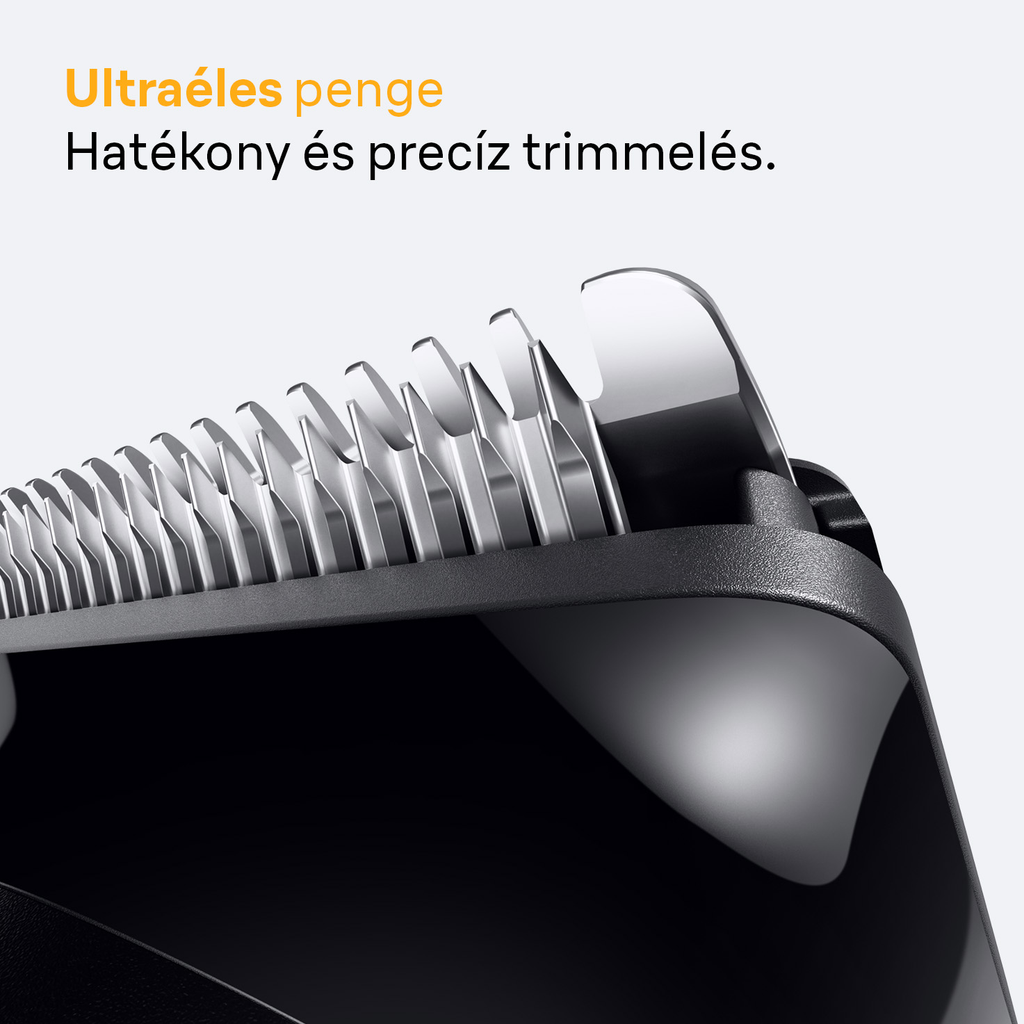 A hajvágógép pengéjének közeli képe. Ezüst pengék láthatók, fekete műanyag testtel, fehér háttér előtt.