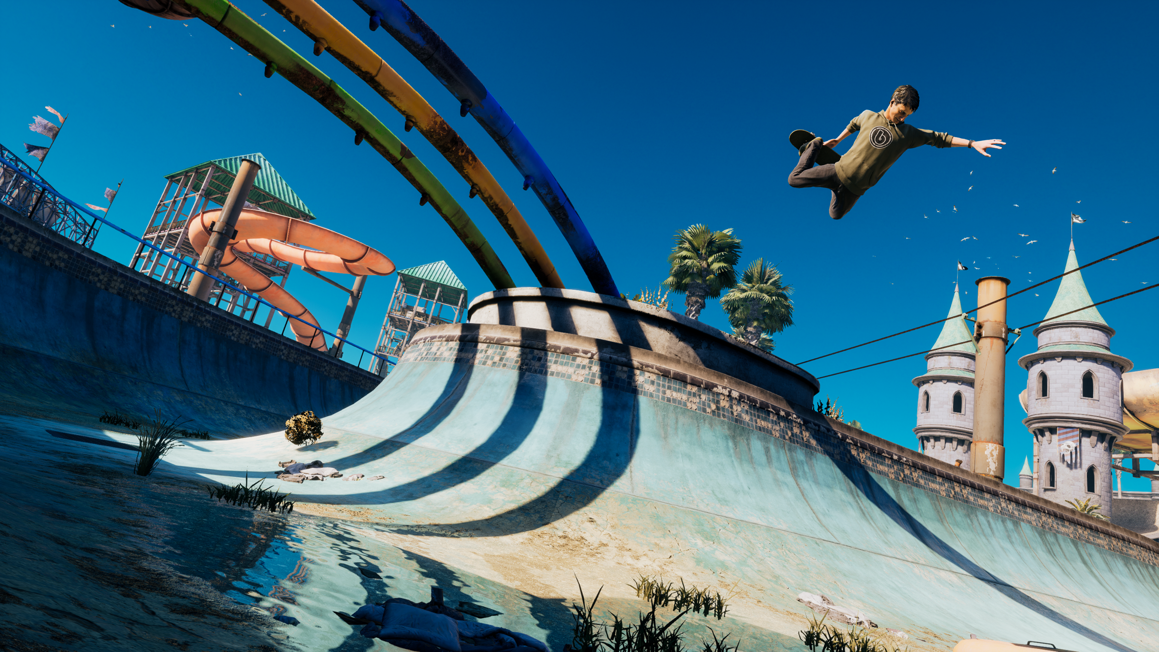 Uno skater salta sopra uno skatepark. Sullo sfondo ci sono scivoli d'acqua e una struttura simile a un castello sotto un cielo blu.