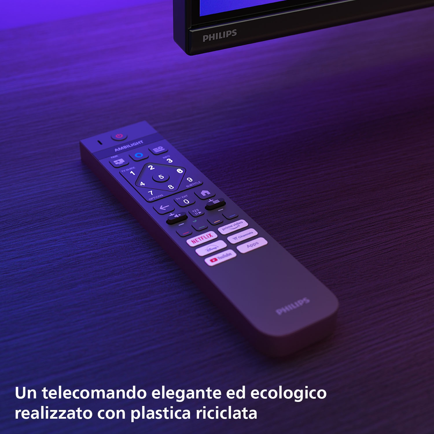 Un telecomando scuro su un tavolo di legno con un televisore Philips sullo sfondo. Il telecomando ha pulsanti e loghi.