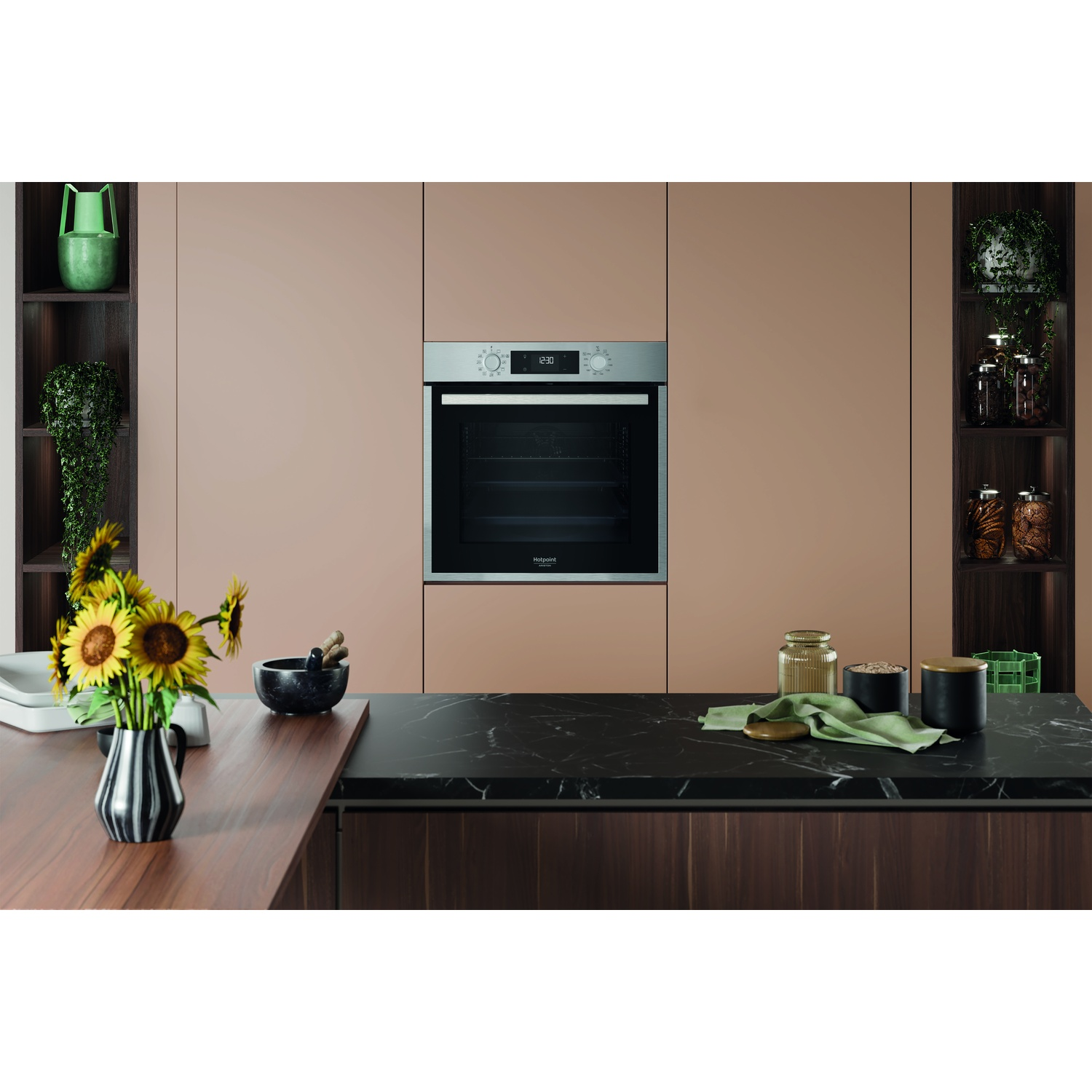 Una cucina con forno, girasoli e piano di lavoro nero. Scaffali laterali con piante e barattoli. La combinazione di colori è marrone e beige.