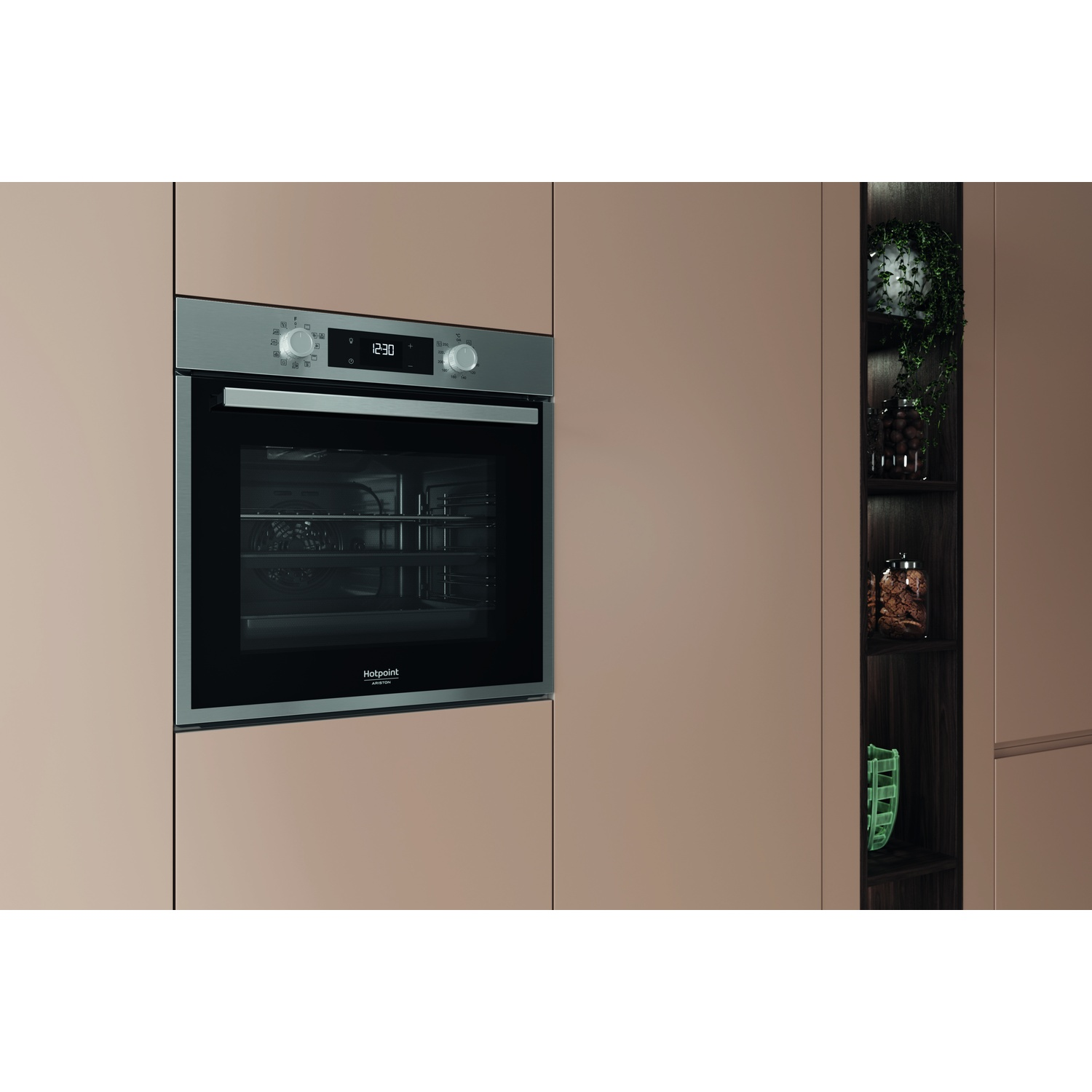 Un forno Hotpoint a incasso con orologio digitale in una cucina. Ripiani a destra mostrano piante e barattoli. Il colore è beige.