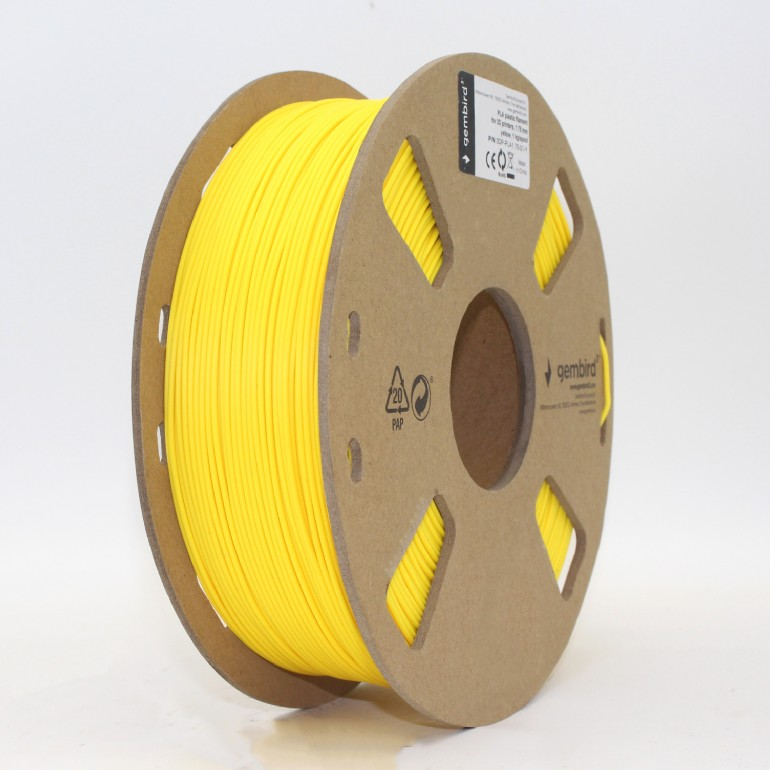 Egy sárga filament orsó 3D nyomtatókhoz fehér felületen. Az orsó sárga műanyagból készült, barna kartonkerettel.