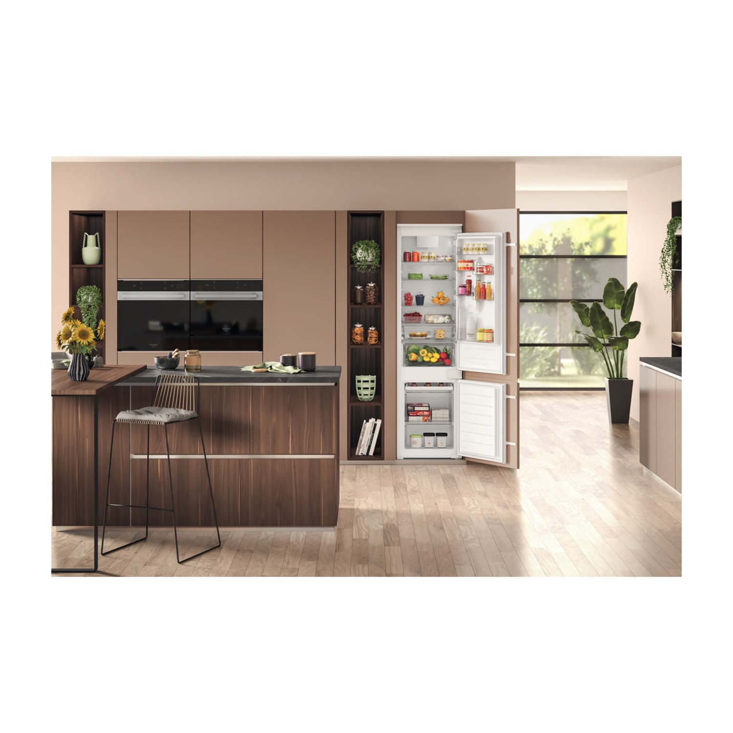 Cucina moderna con frigorifero aperto. Include sgabello, fiori, forni a incasso e vari alimenti. Sono presenti mobili in legno.