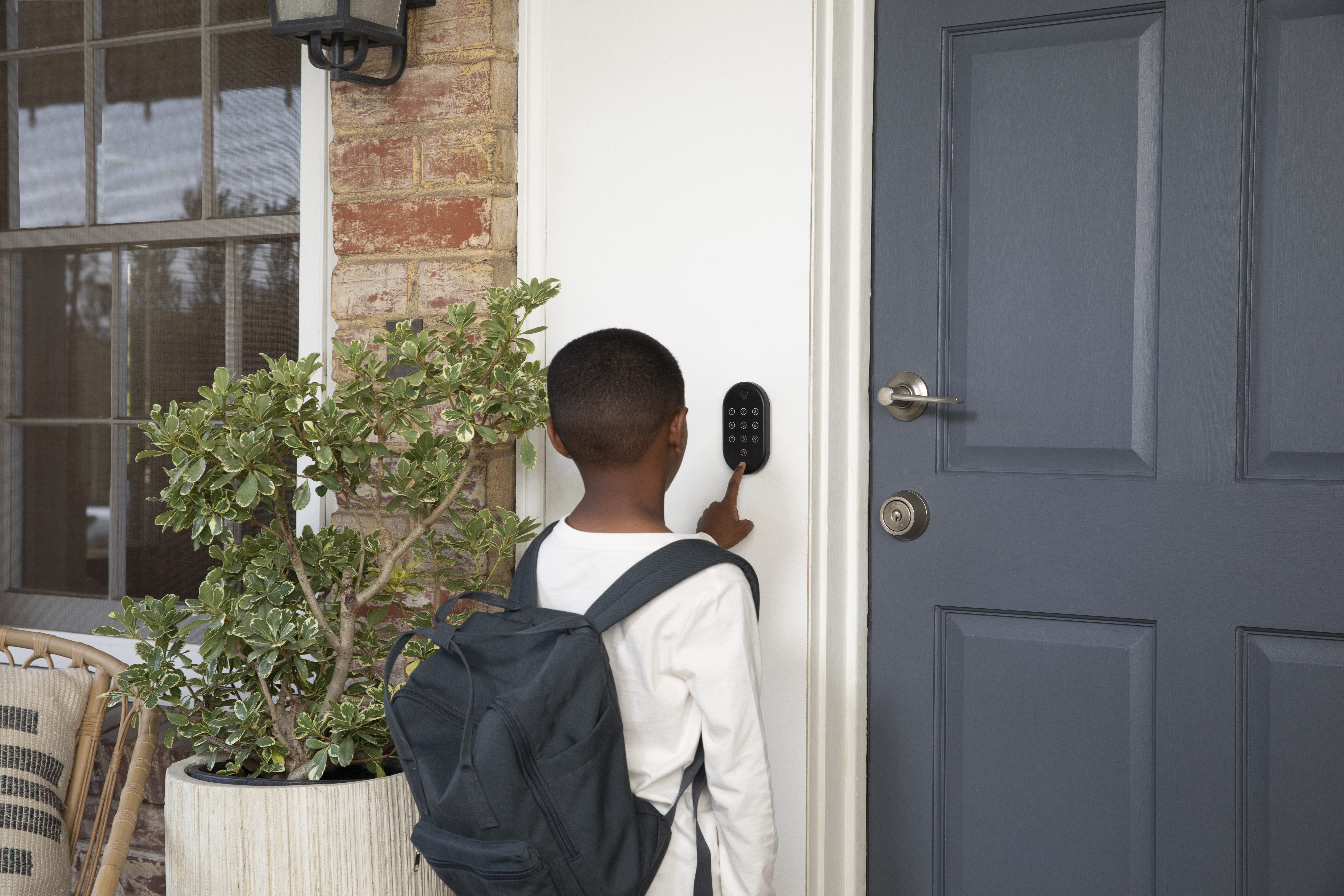 Ein Kind mit Rucksack benutzt ein Tastenfeld, um eine Tür zu öffnen. Links steht eine Pflanze, rechts eine blaue Tür.