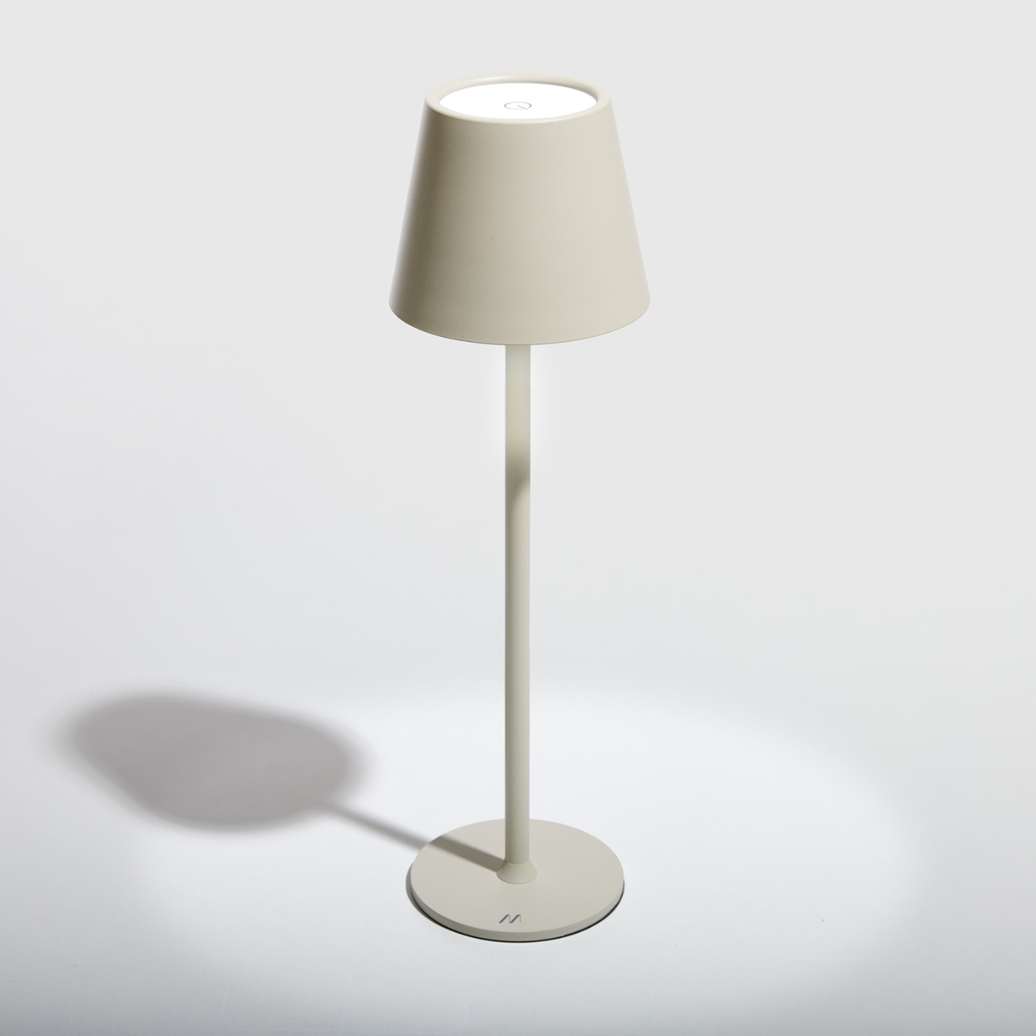 Una lampada beige con paralume conico su una superficie bianca. La lampada proietta un'ombra.