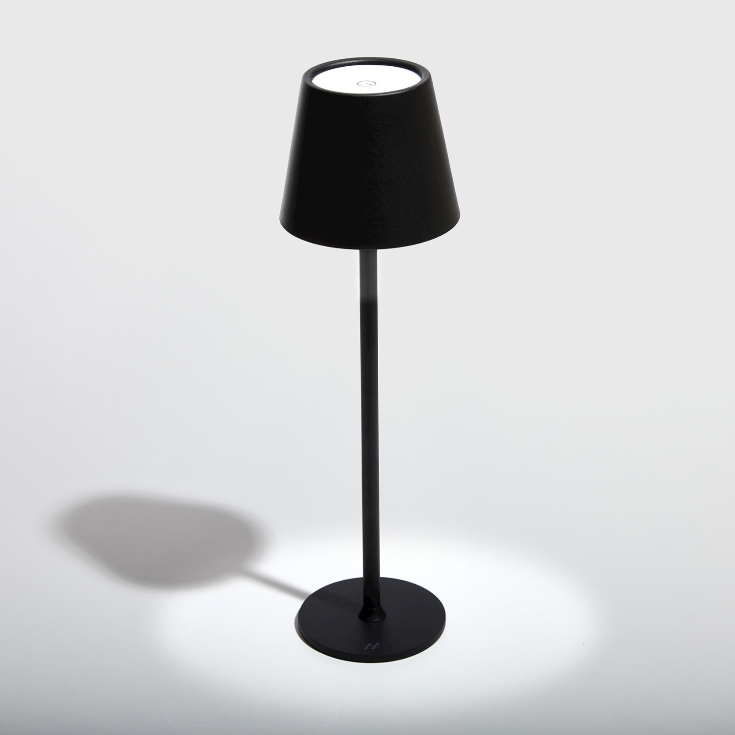 Una lampada nera con un paralume conico su una superficie bianca. Vi è un'ombra della lampada.
