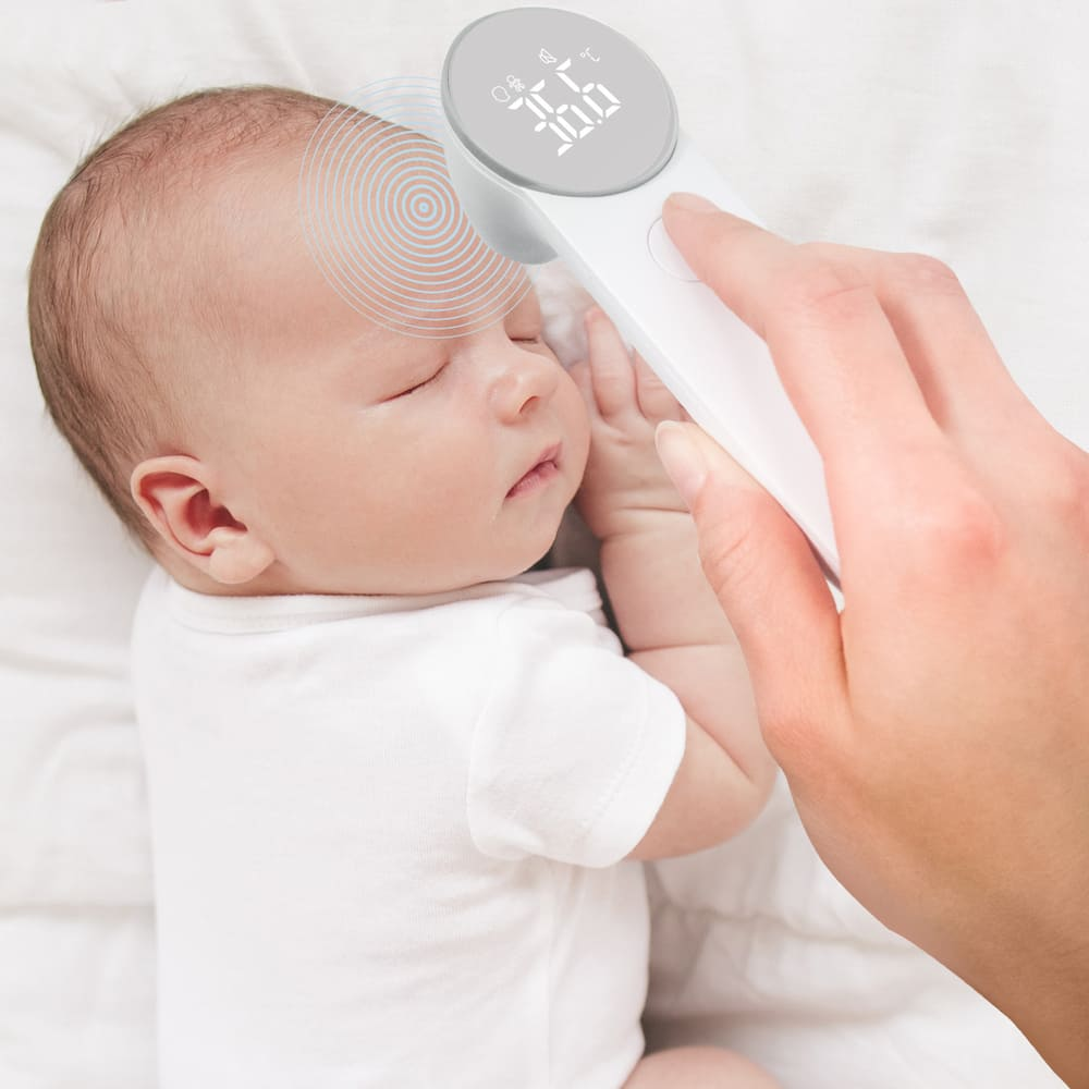 Dziecku mierzy się temperaturę termometrem cyfrowym. Dziecko śpi na białej pościeli. Ręka trzyma termometr.