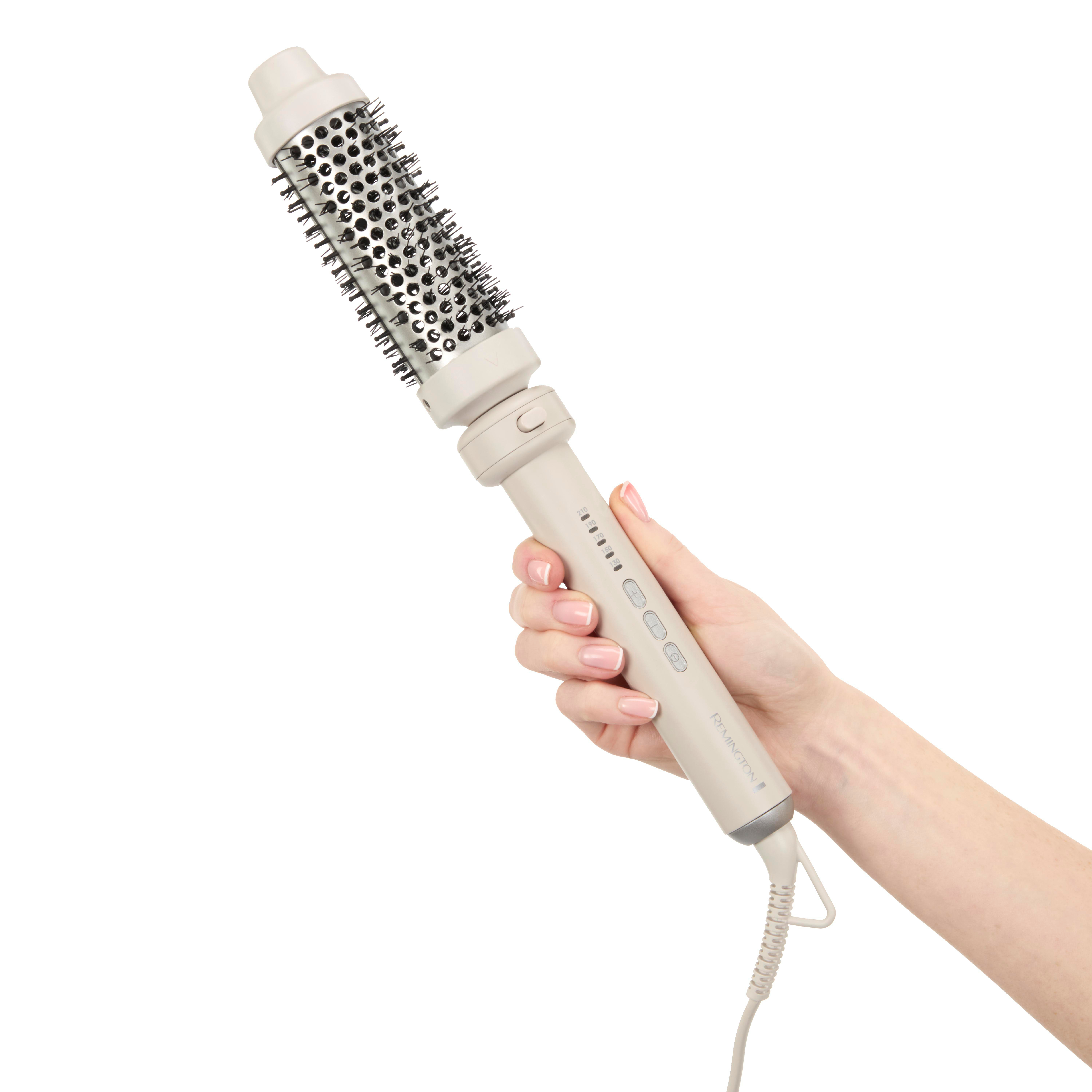 Eine Hand hält eine beige Haarstylingbürste mit rundem, borstenbesetztem Kopf und Kabel. Der Hintergrund ist weiß.