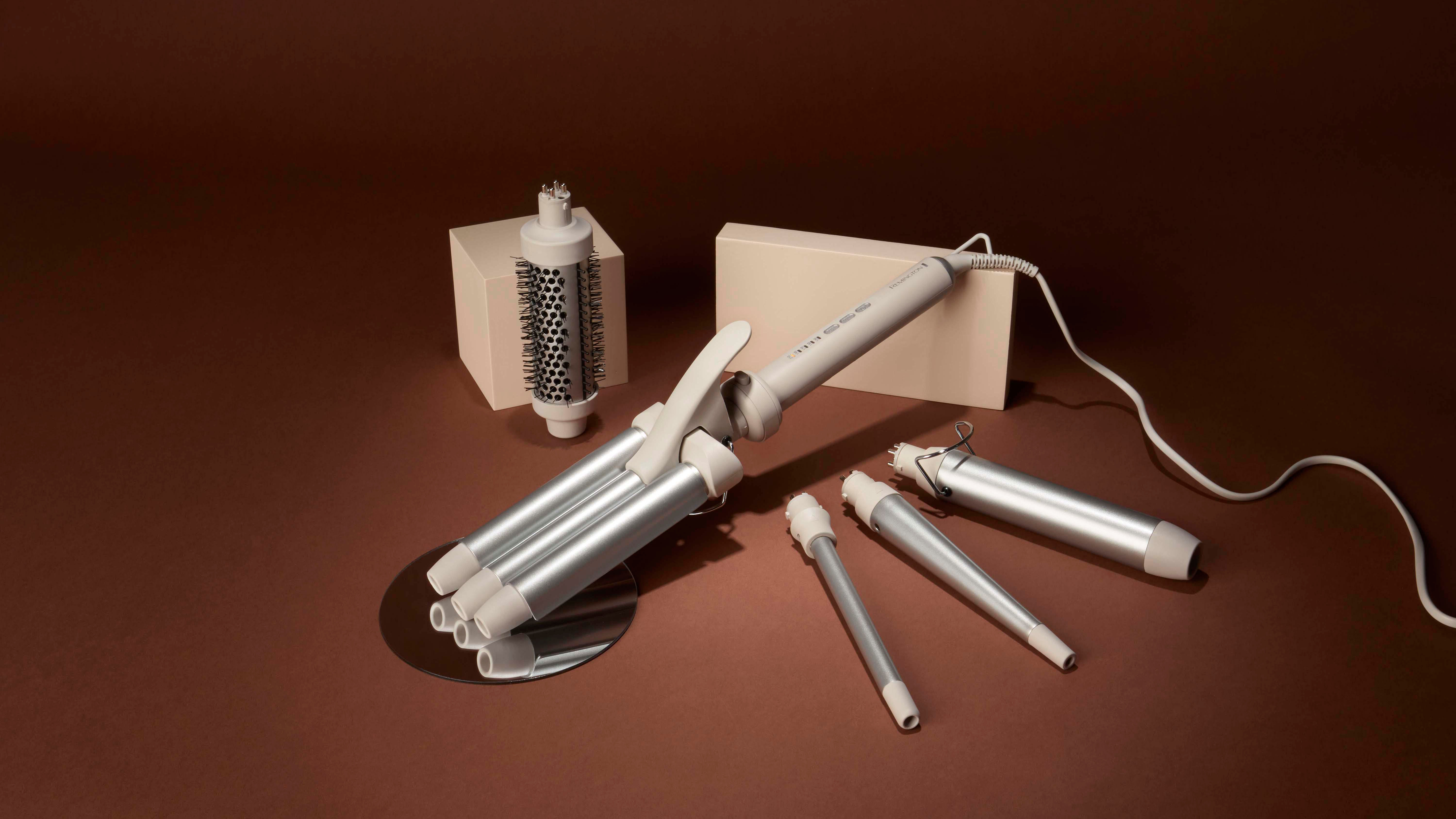 Ein Haarstyling-Set auf braunem Untergrund. Es enthält einen Lockenstab, austauschbare Aufsätze und einen Bürstenaufsatz.