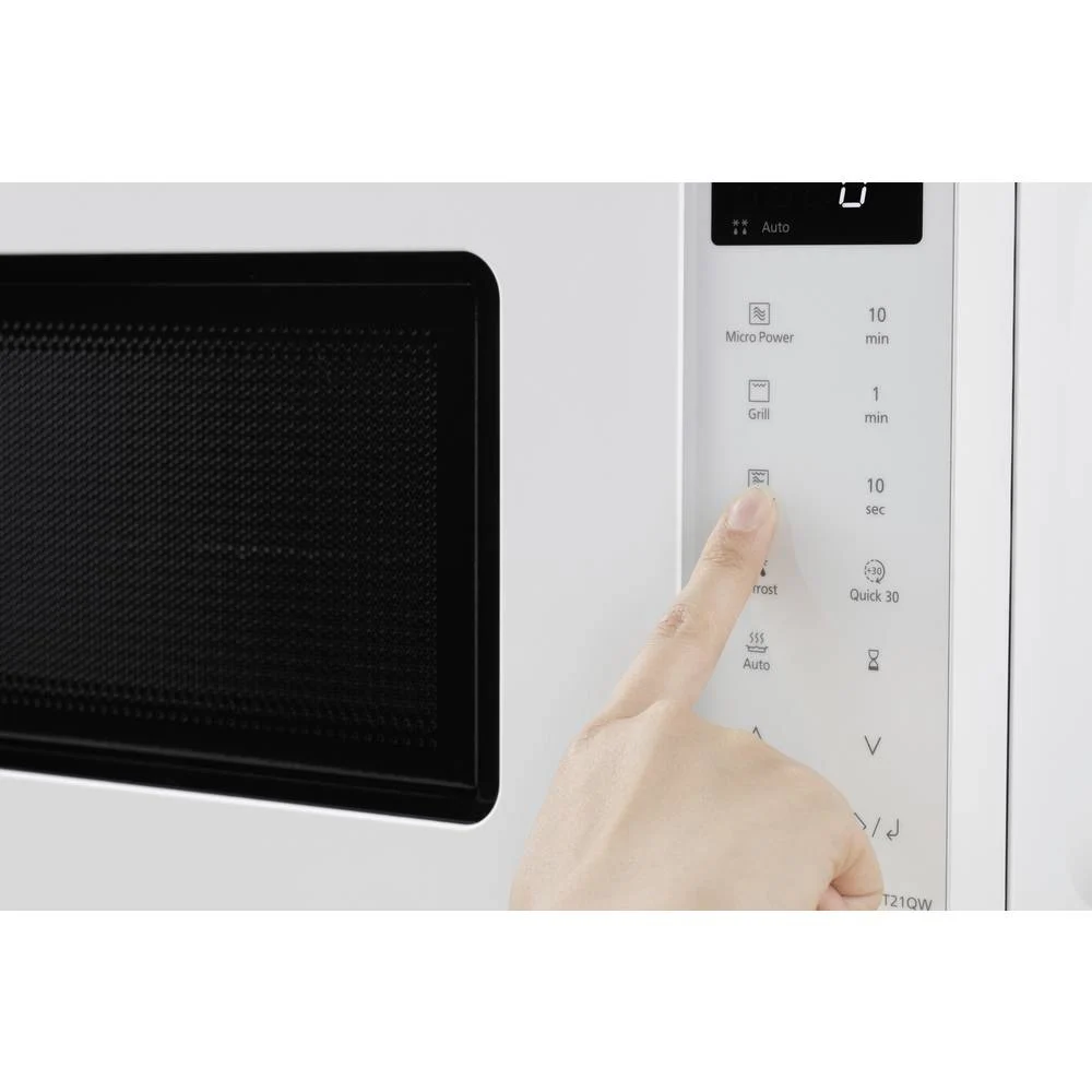 Ręka naciska przycisk 'Odmrażanie' na białej kuchence mikrofalowej z czarną kratką. Wyświetlacz pokazuje ustawienia czasu.