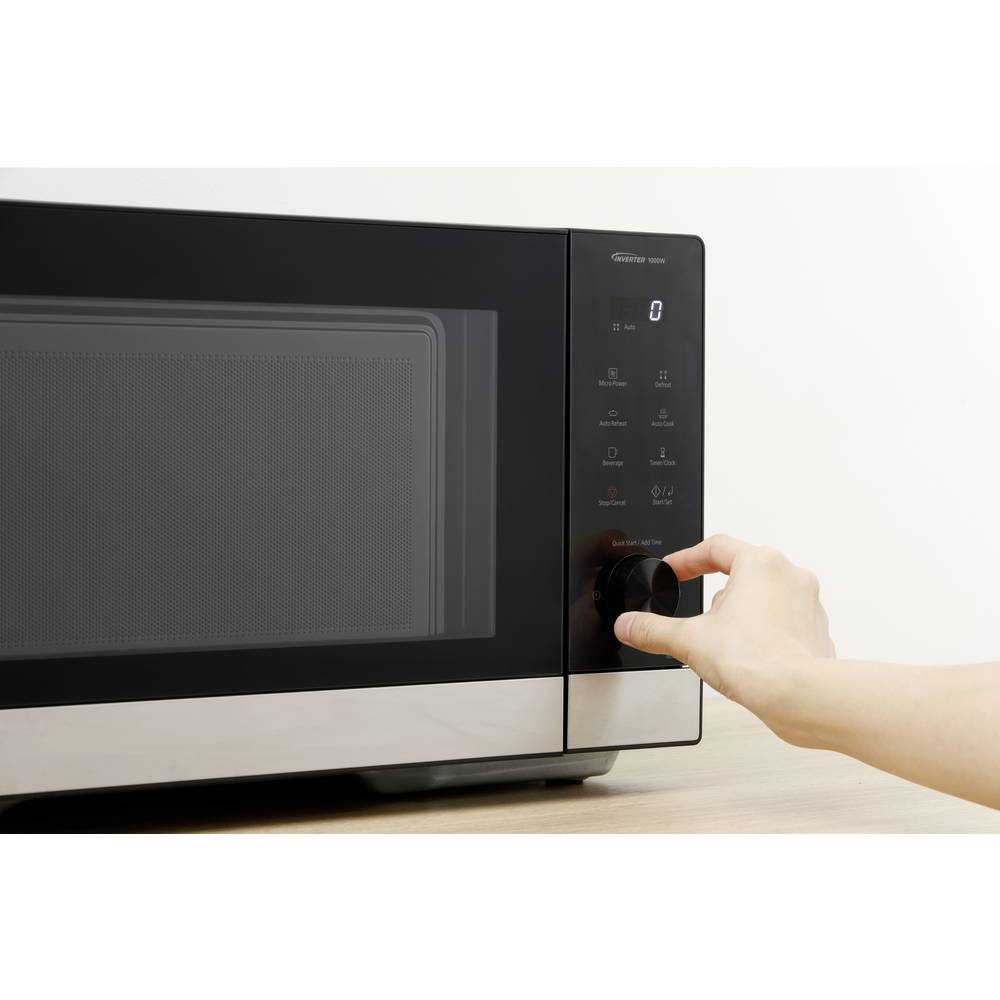 Dłoń obraca pokrętło kuchenki mikrofalowej. Kuchenka mikrofalowa jest czarna i srebrna z cyfrowym wyświetlaczem.