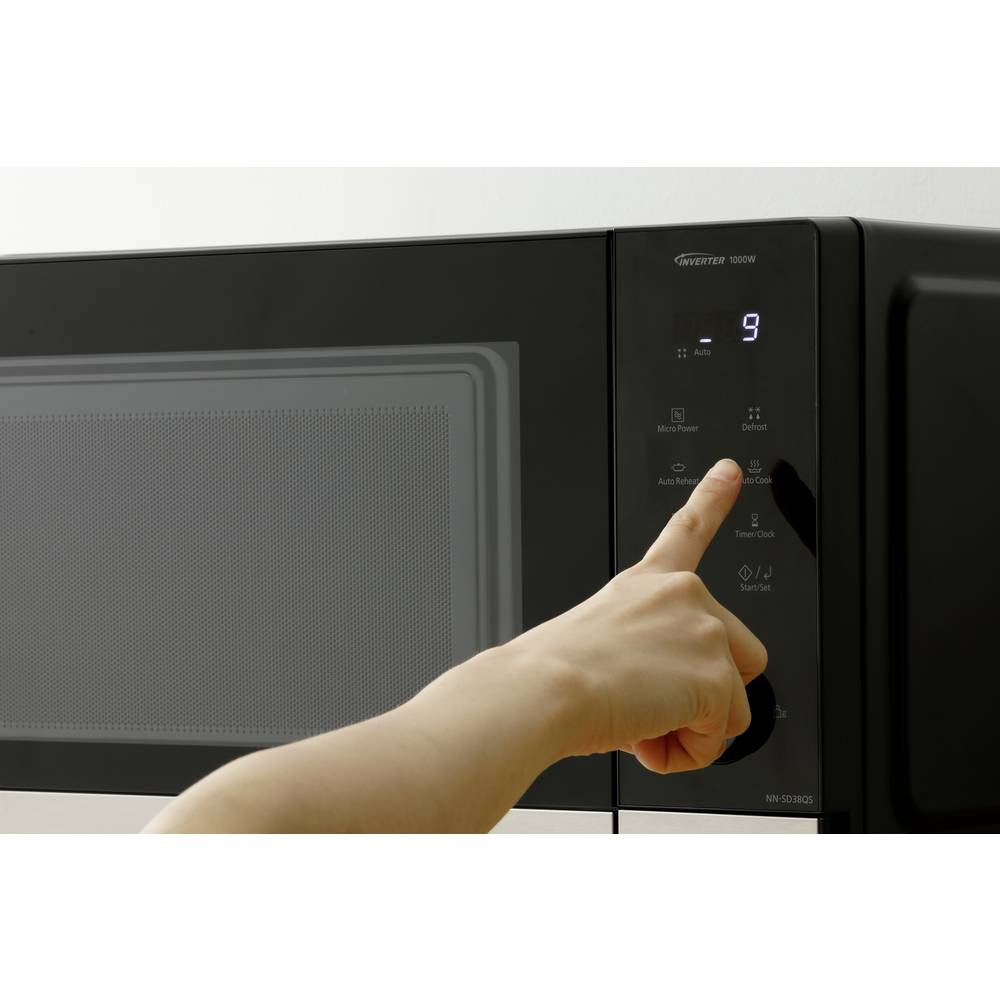 Ręka naciska przycisk na czarnej kuchence mikrofalowej. Kuchenka mikrofalowa ma cyfrowy wyświetlacz z '9'.