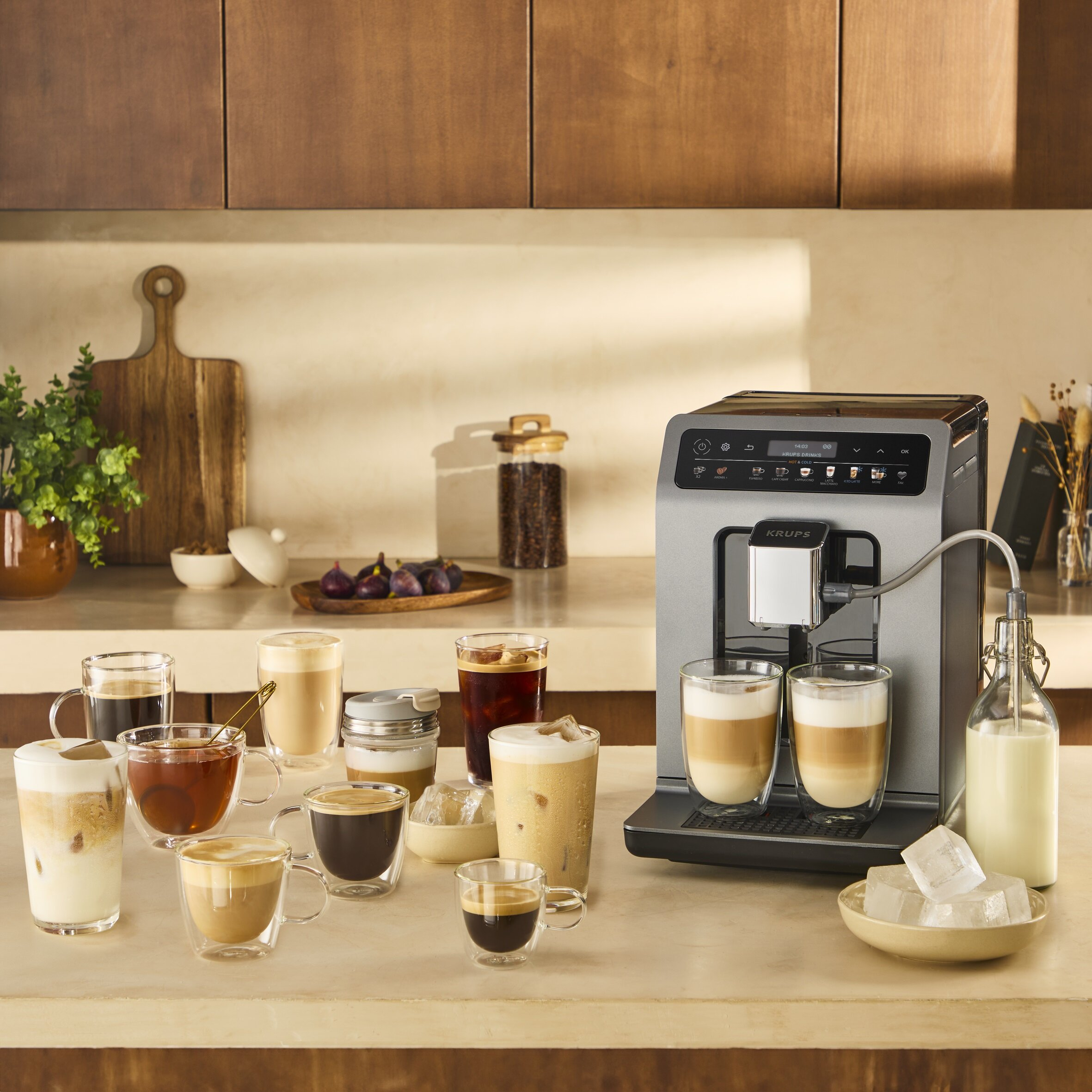 Ekspres do kawy z różnymi napojami kawowymi w szklankach. Kostki lodu i butelka mleka na stole. Drewniane szafki w tle.