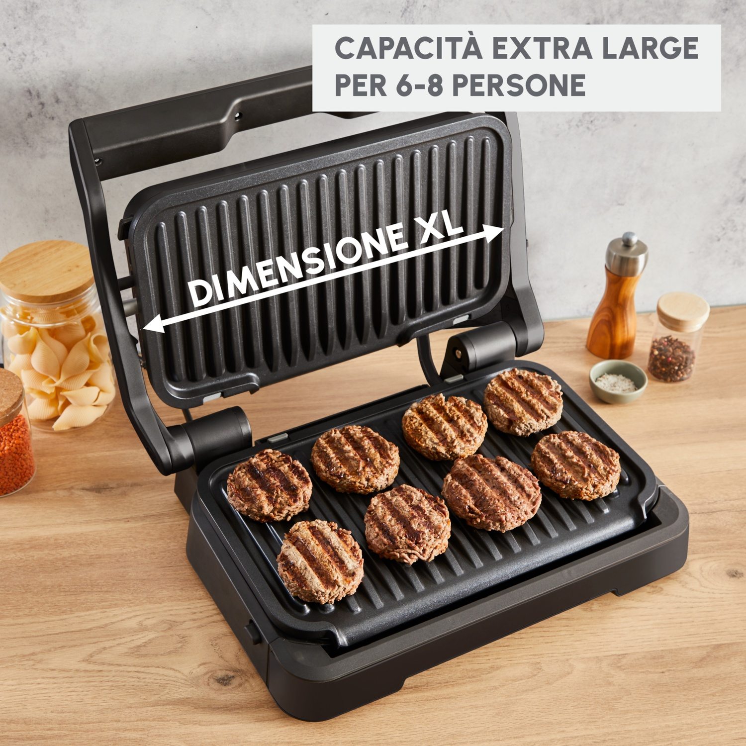 Una griglia nera aperta con hamburger cotti. A sinistra, un barattolo di pasta e lenticchie. A destra, un macinapepe e spezie.
