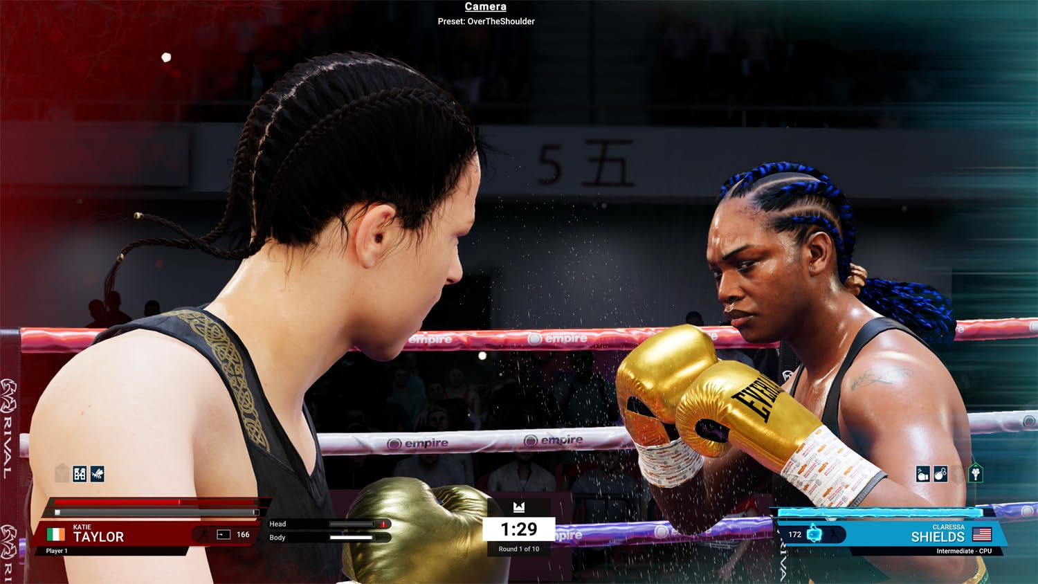 Due pugili donne si affrontano sul ring. Una ha trecce nere, l'altra blu. Guanti d'oro e il timer sono visibili.