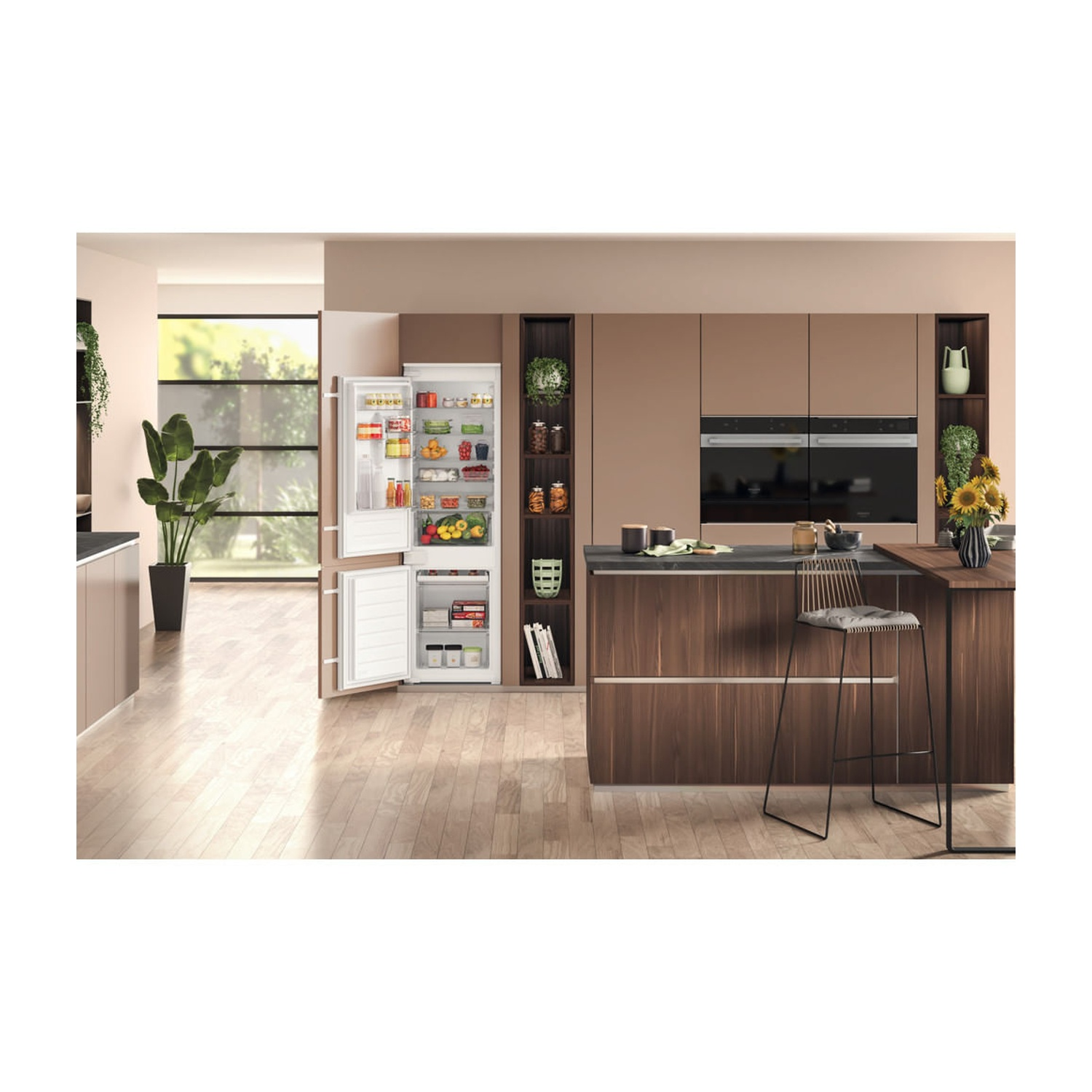 Scena cucina con frigorifero aperto, mobili in legno e bar con sgabelli. Piante e girasoli aggiungono colore.