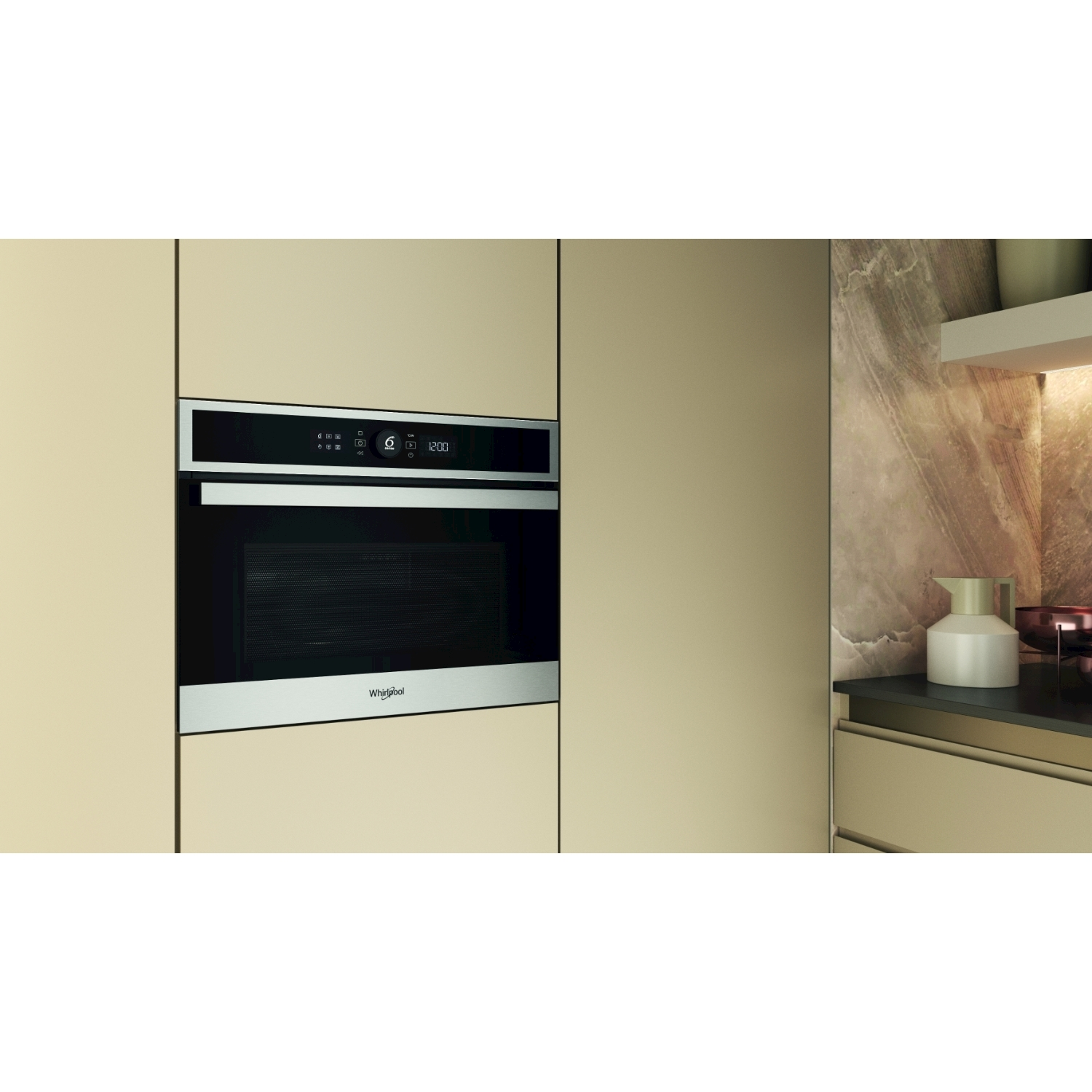 Un forno Whirlpool a incasso è centrato su una parete color crema. Una brocca bianca e una ciotola di rame sono su un piano di lavoro.