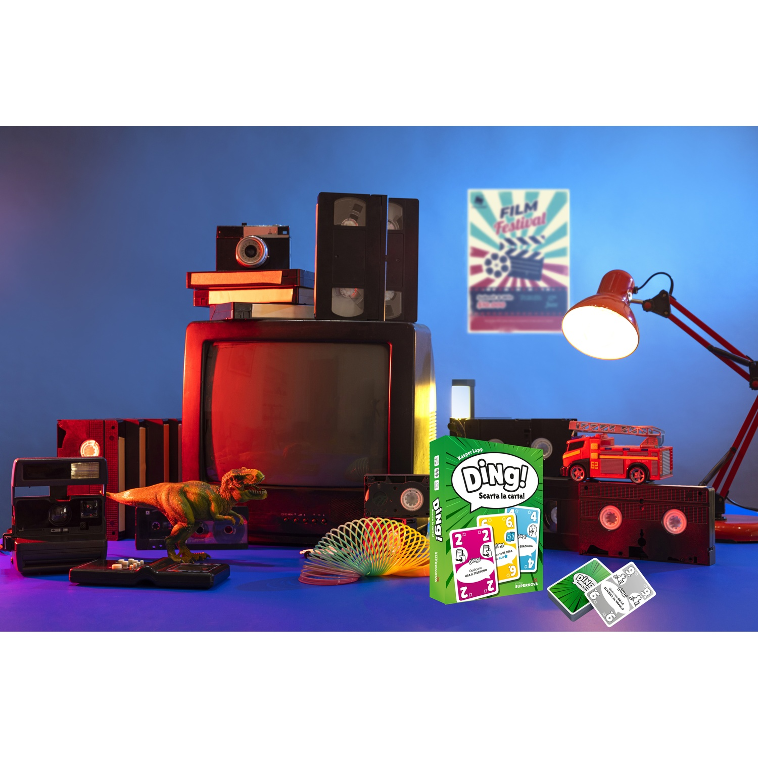 Una scena retrò con TV, videocassette, fotocamere, un dinosauro giocattolo e un gioco di carte. Una lampada rossa e un poster di un film sullo sfondo.