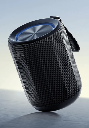 Czarny cylindryczny głośnik o teksturowanej powierzchni. Posiada uchwyt i metalowy wierzch z niebieskim pierścieniem.