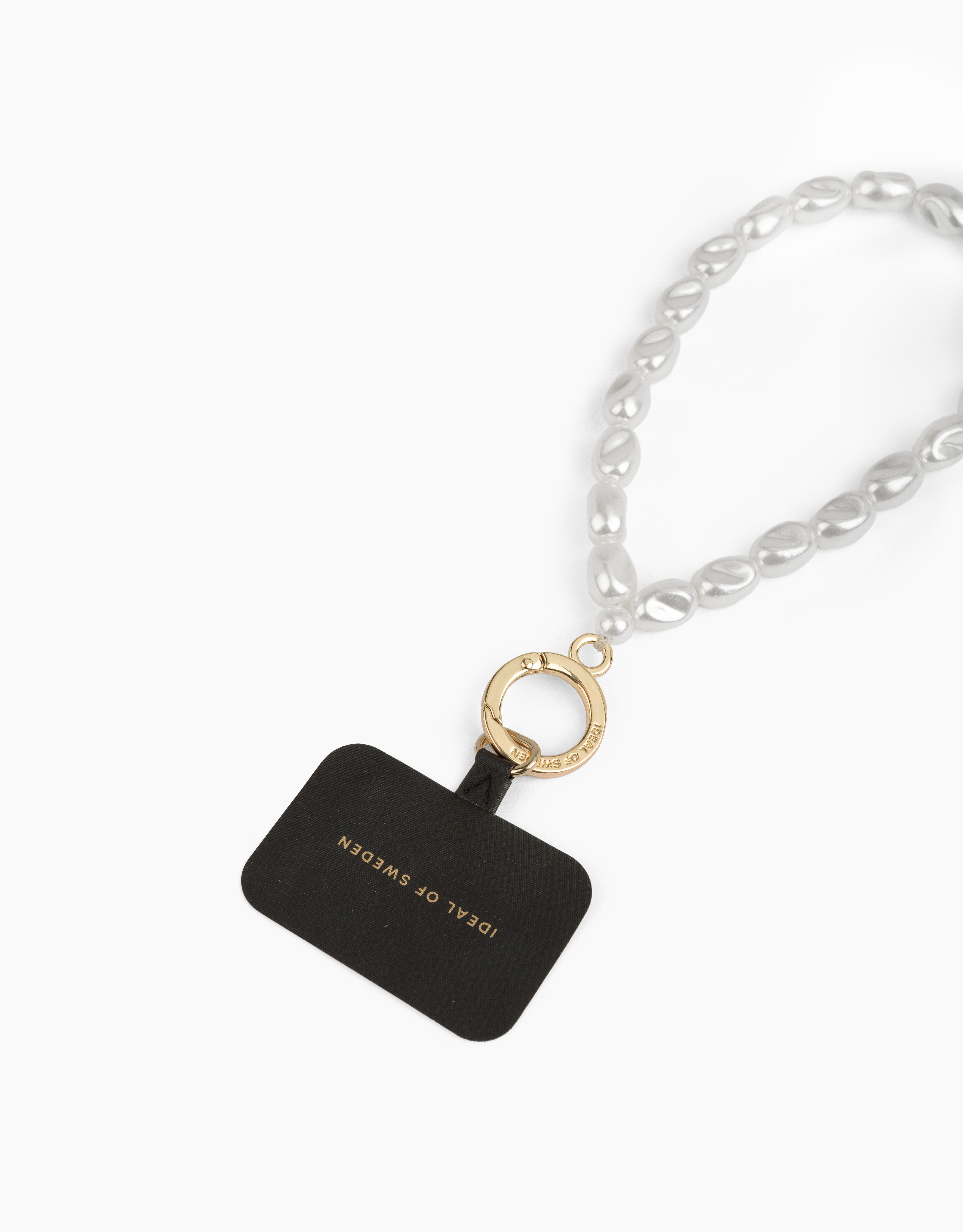 Eine perlenbesetzte Handy-Schlaufe mit goldenem Ring und schwarzem Ideal of Sweden-Anhänger auf weißem Hintergrund.